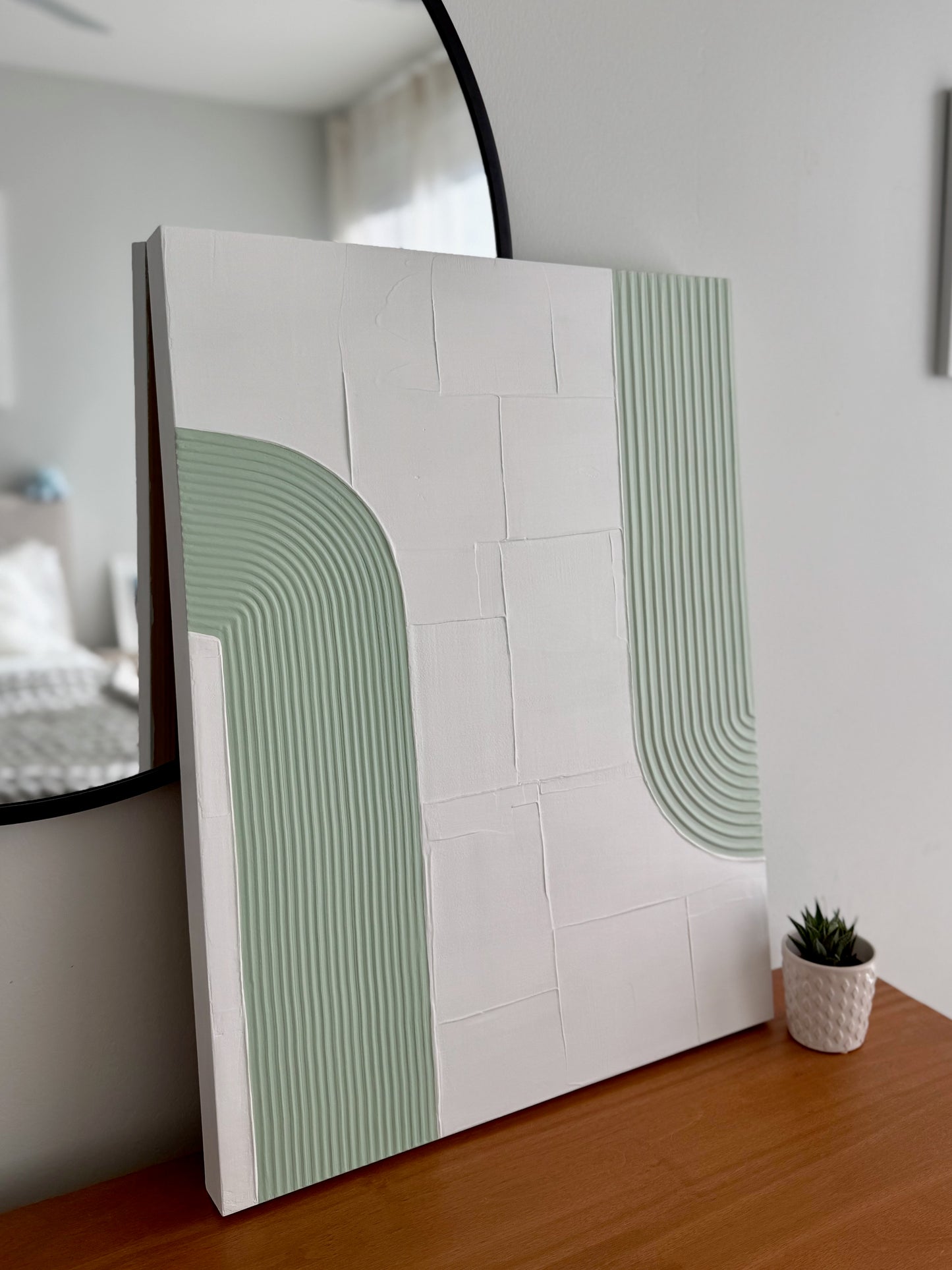 Decorative wall artwork with green abstract design on a white background, placed against a mirror.