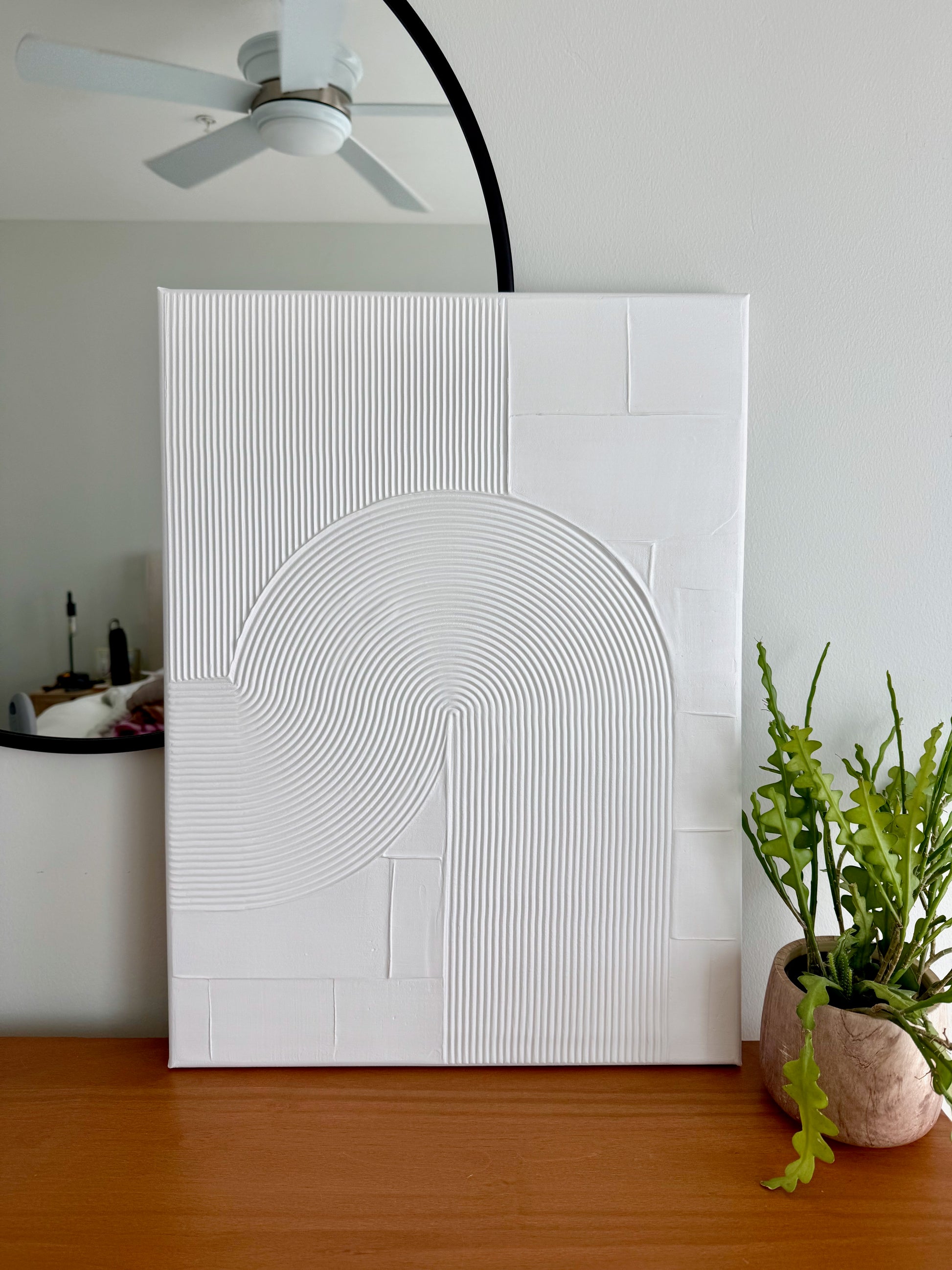 White textured wall art on a wooden surface with a plant in the background