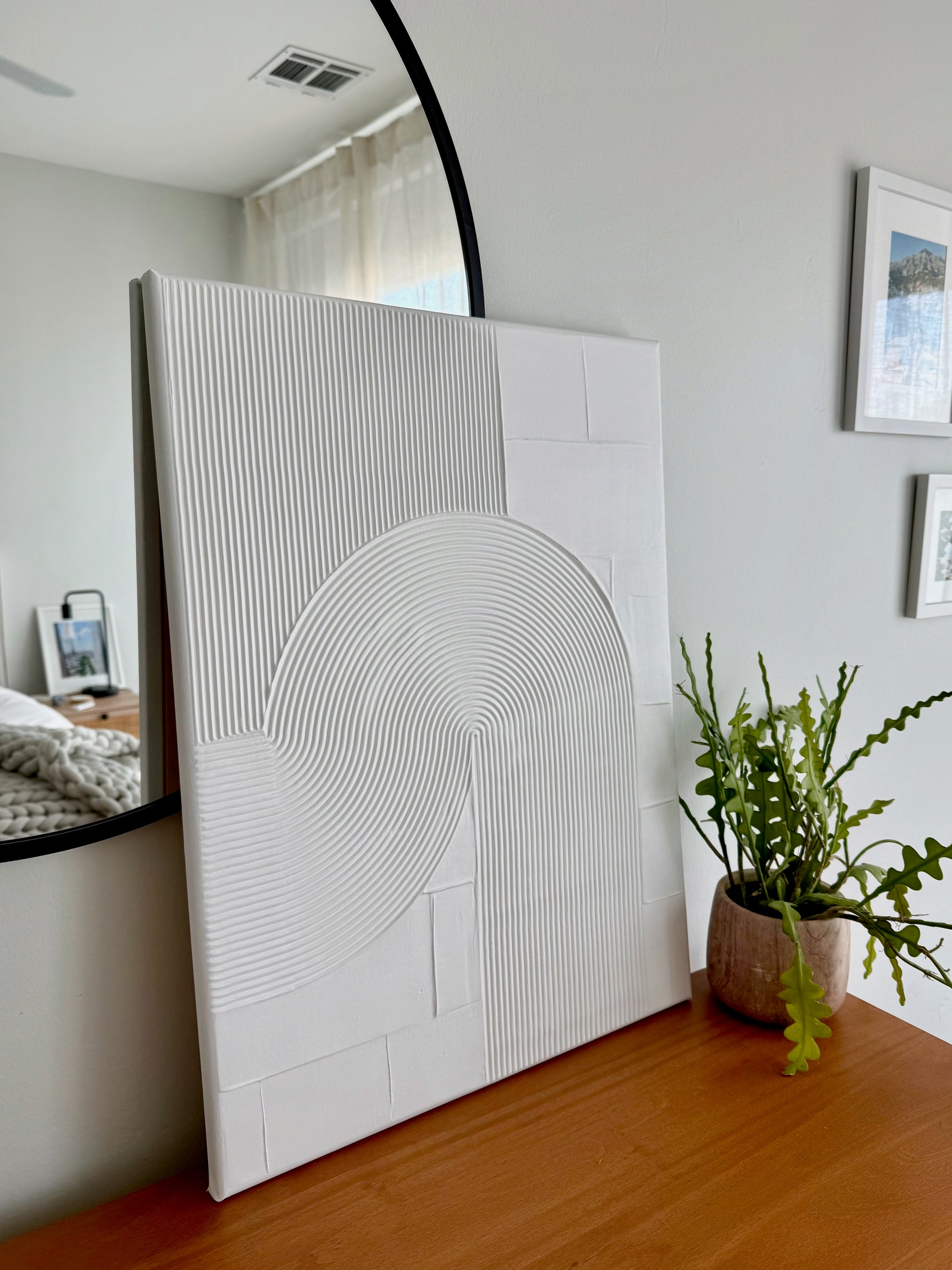 White textured wall art piece in a room with a plant and mirror.