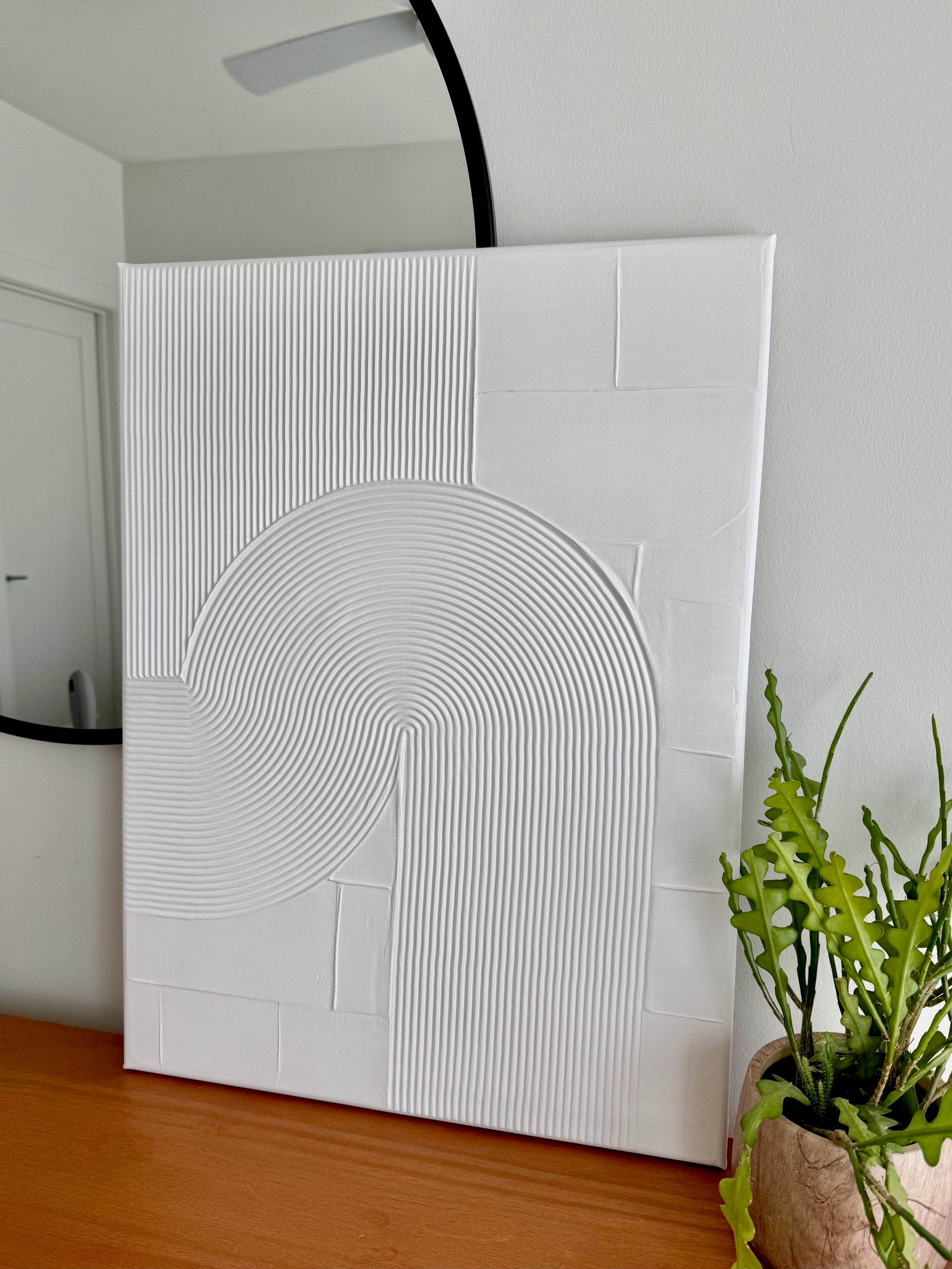 White textured wall art on a wooden surface with a plant in the background