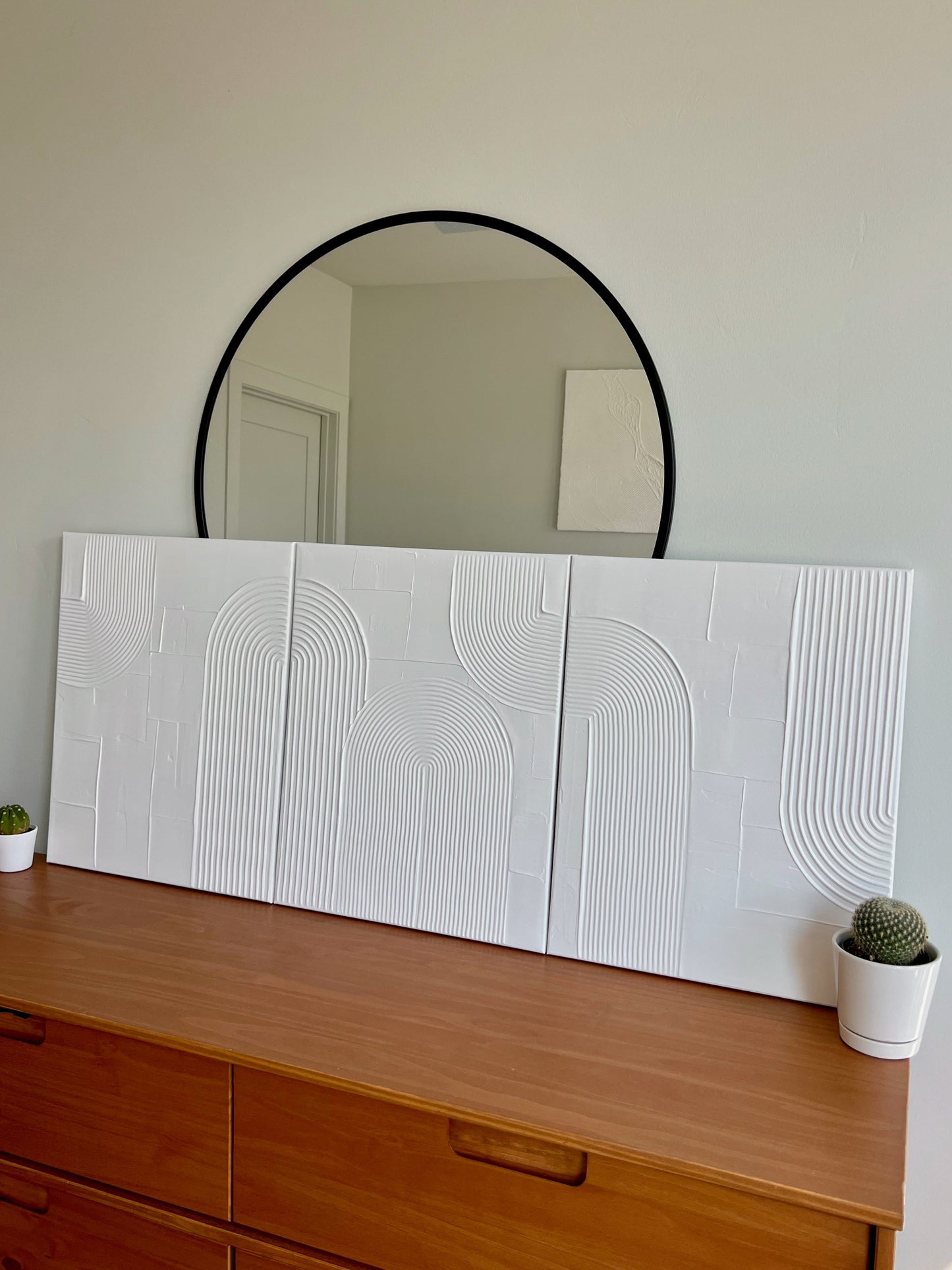 Wooden dresser with a large decorative mirror and two small potted plants.