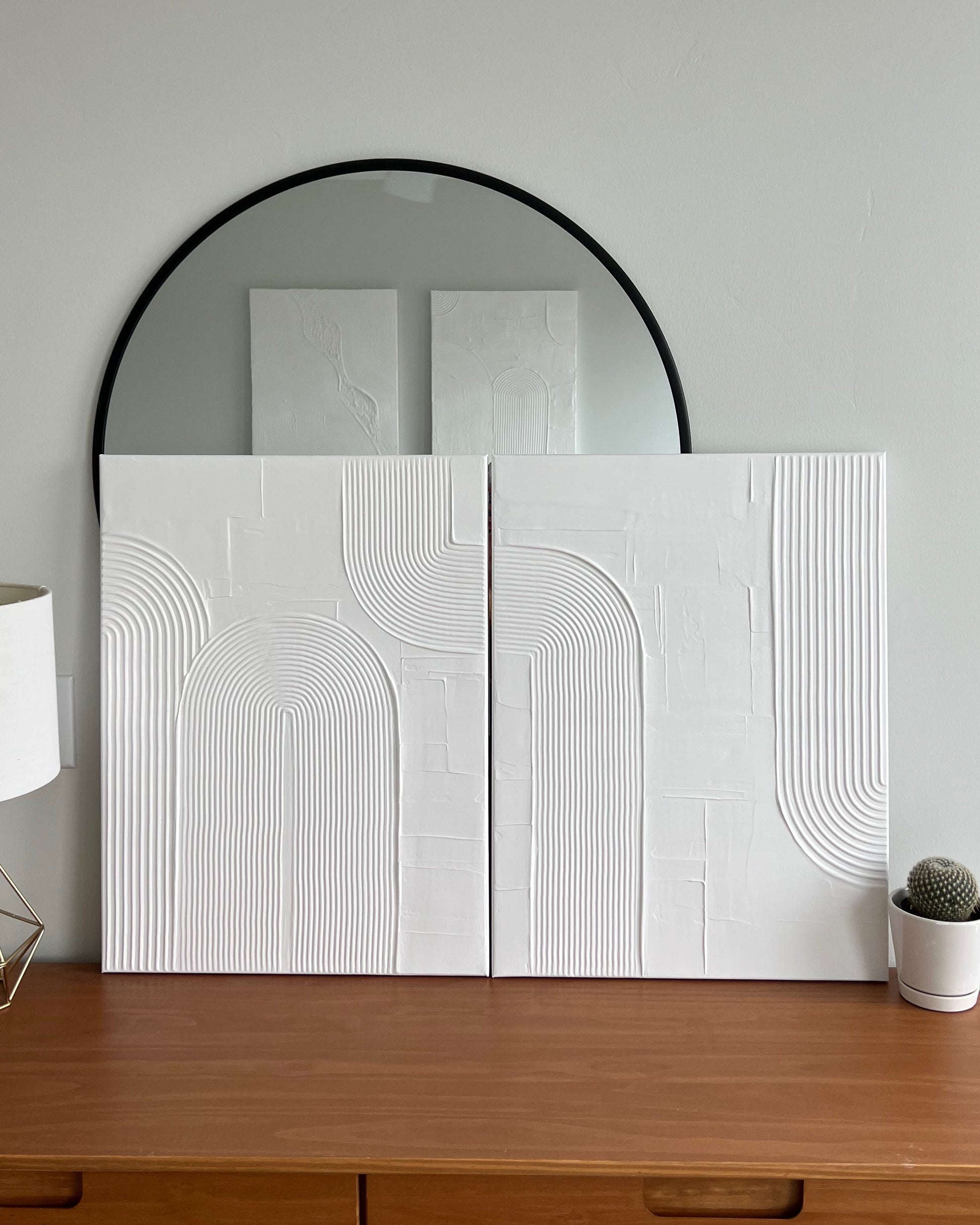 Wooden dresser with a large round mirror above it, featuring a white textured wall panel.