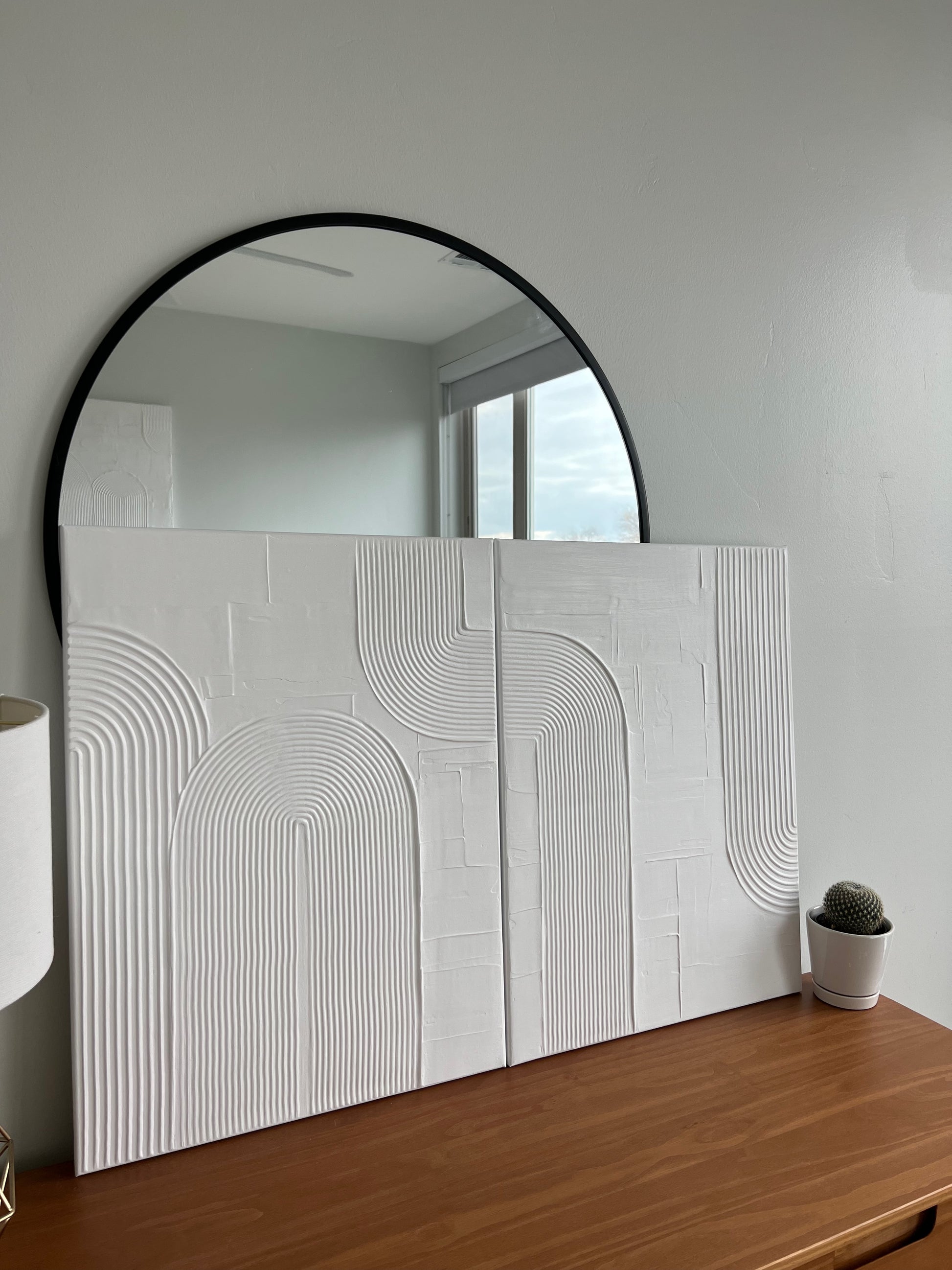 Round mirror on a wall with a decorative white panel below