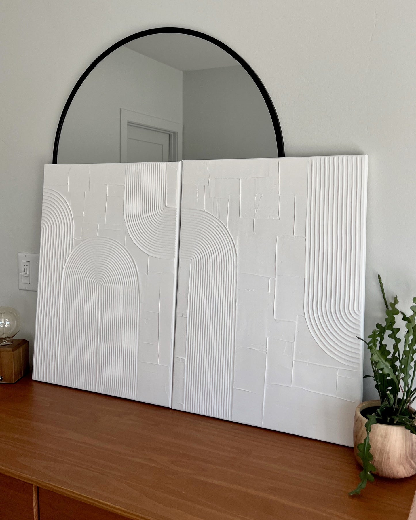 White textured wall art on a wooden surface with a round mirror above it.