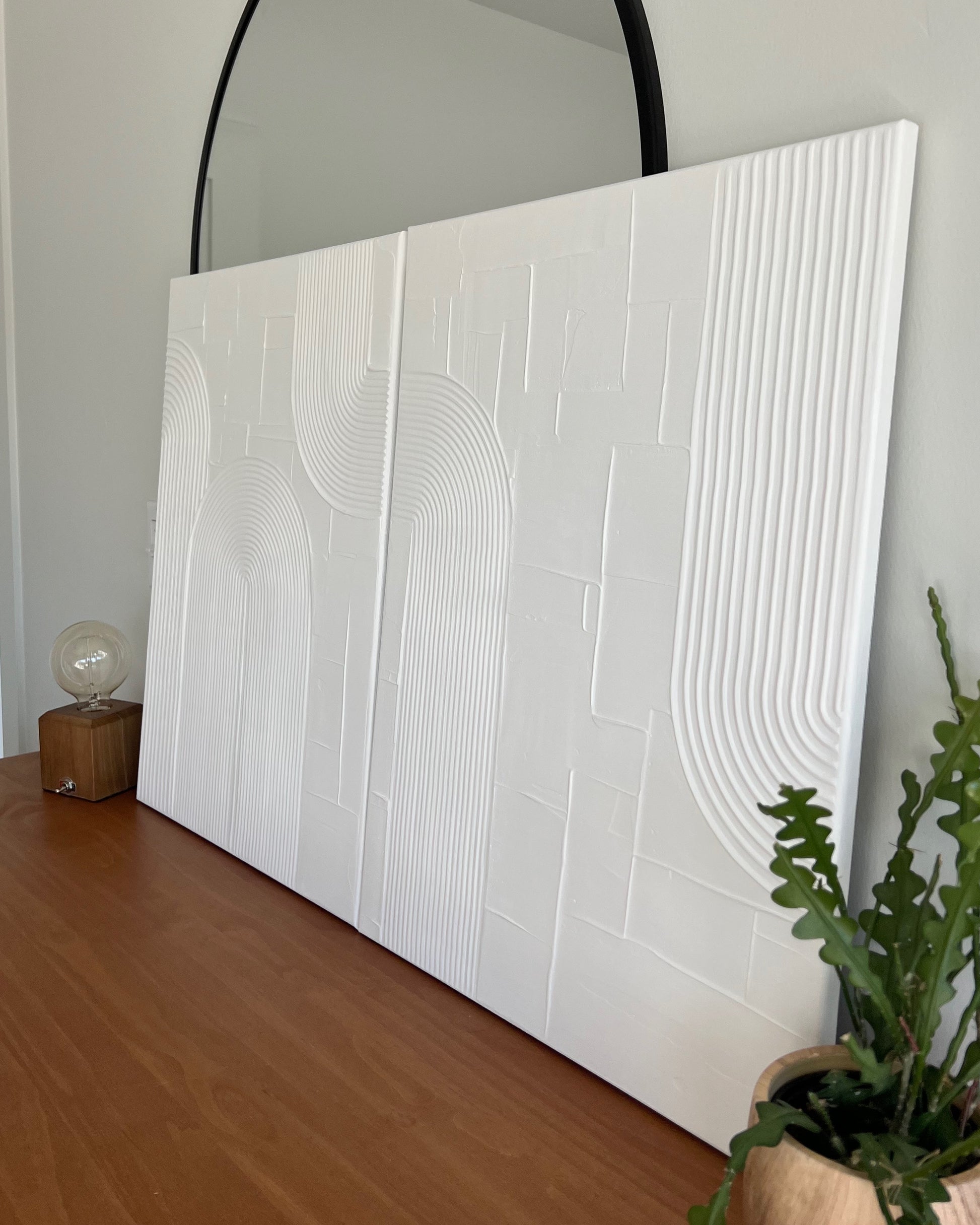 White textured wall art piece on a wooden surface with a mirror above it.