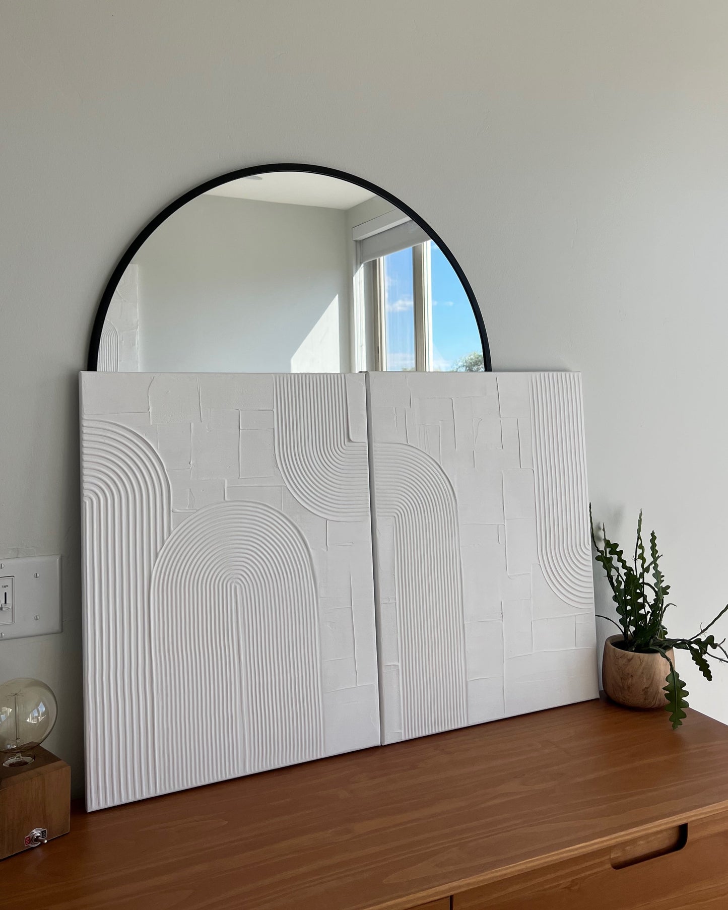 Large round mirror on a wall above a wooden surface with a white textured panel.