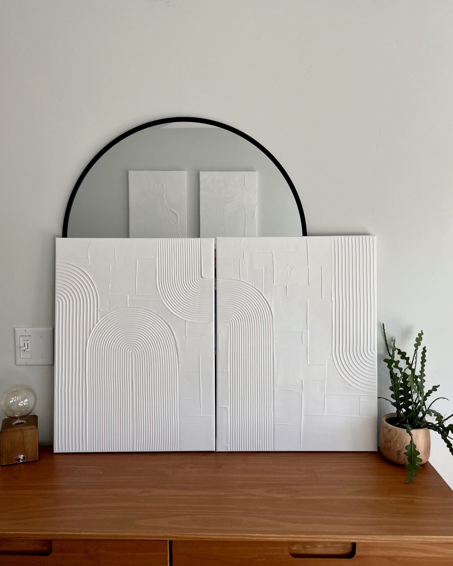 White textured wall panels with a round mirror above on a light gray wall.