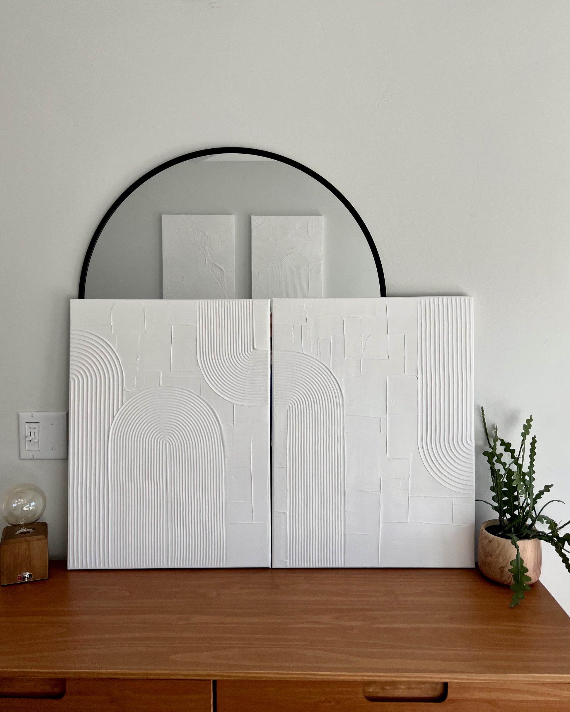White textured wall panels with a round mirror above on a light gray wall.