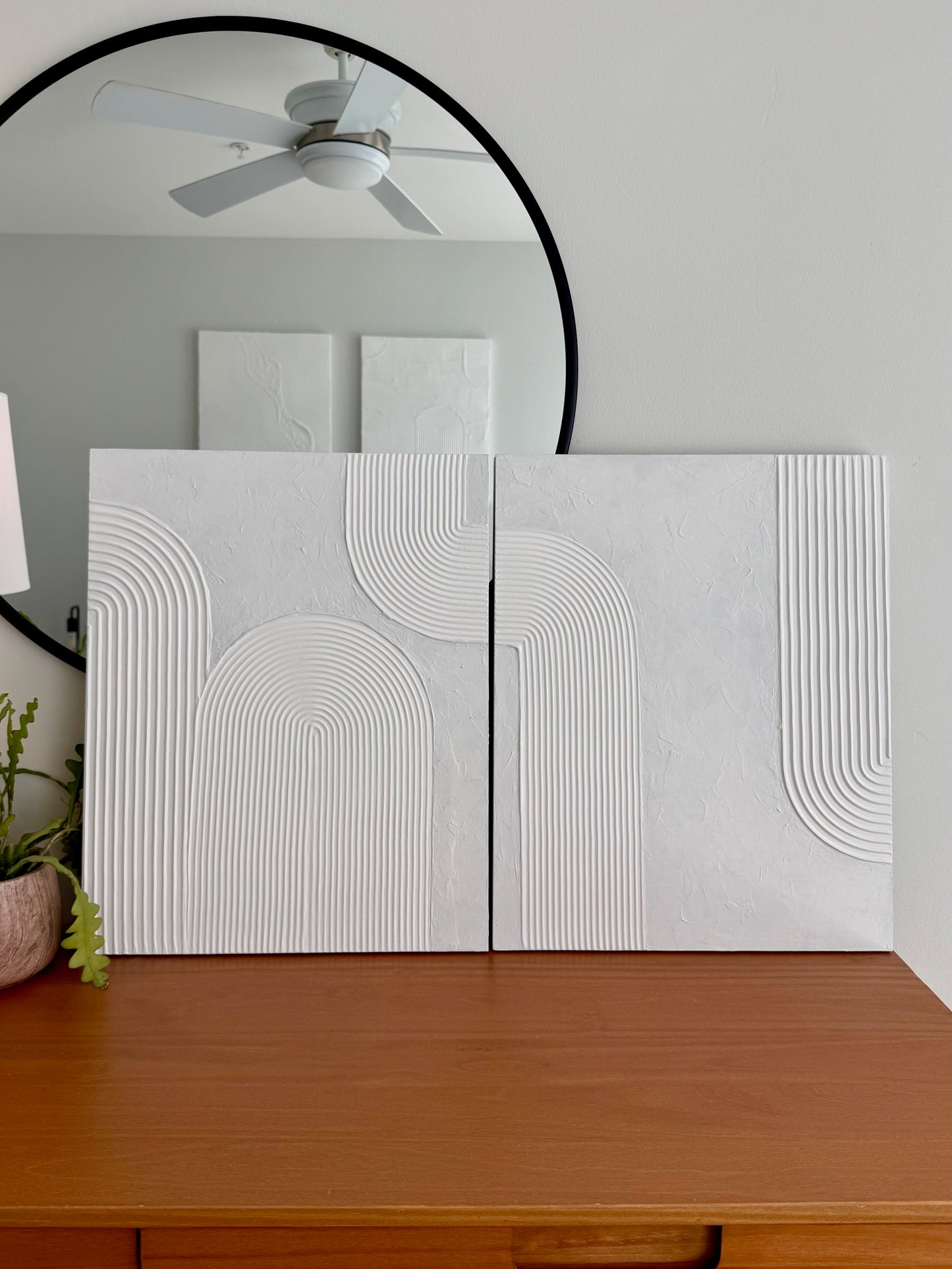 Two white textured wall panels on a wooden surface with a mirror and ceiling fan in the background.