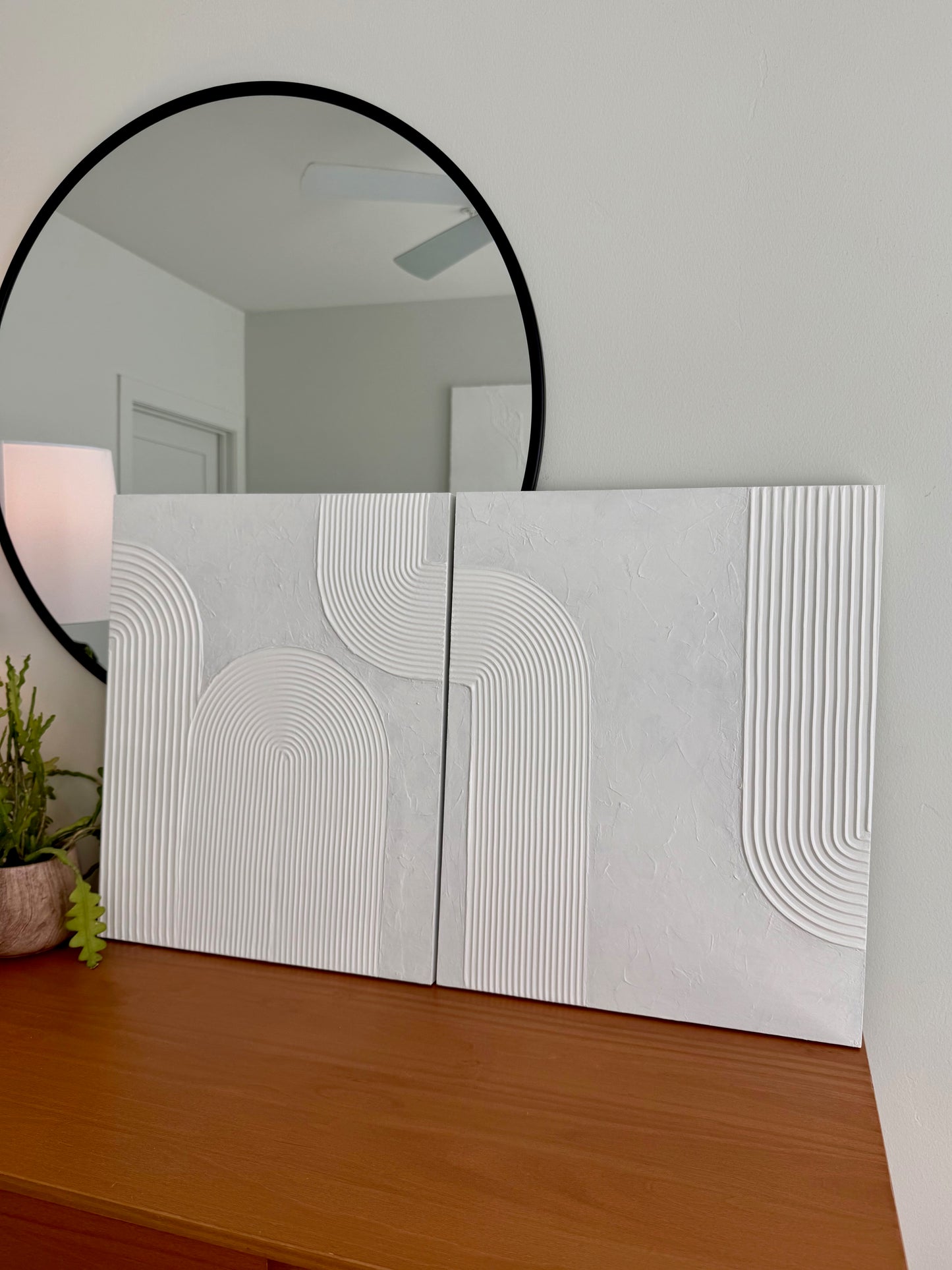Decorative wall art with geometric patterns on a wooden surface, featuring a round mirror above.