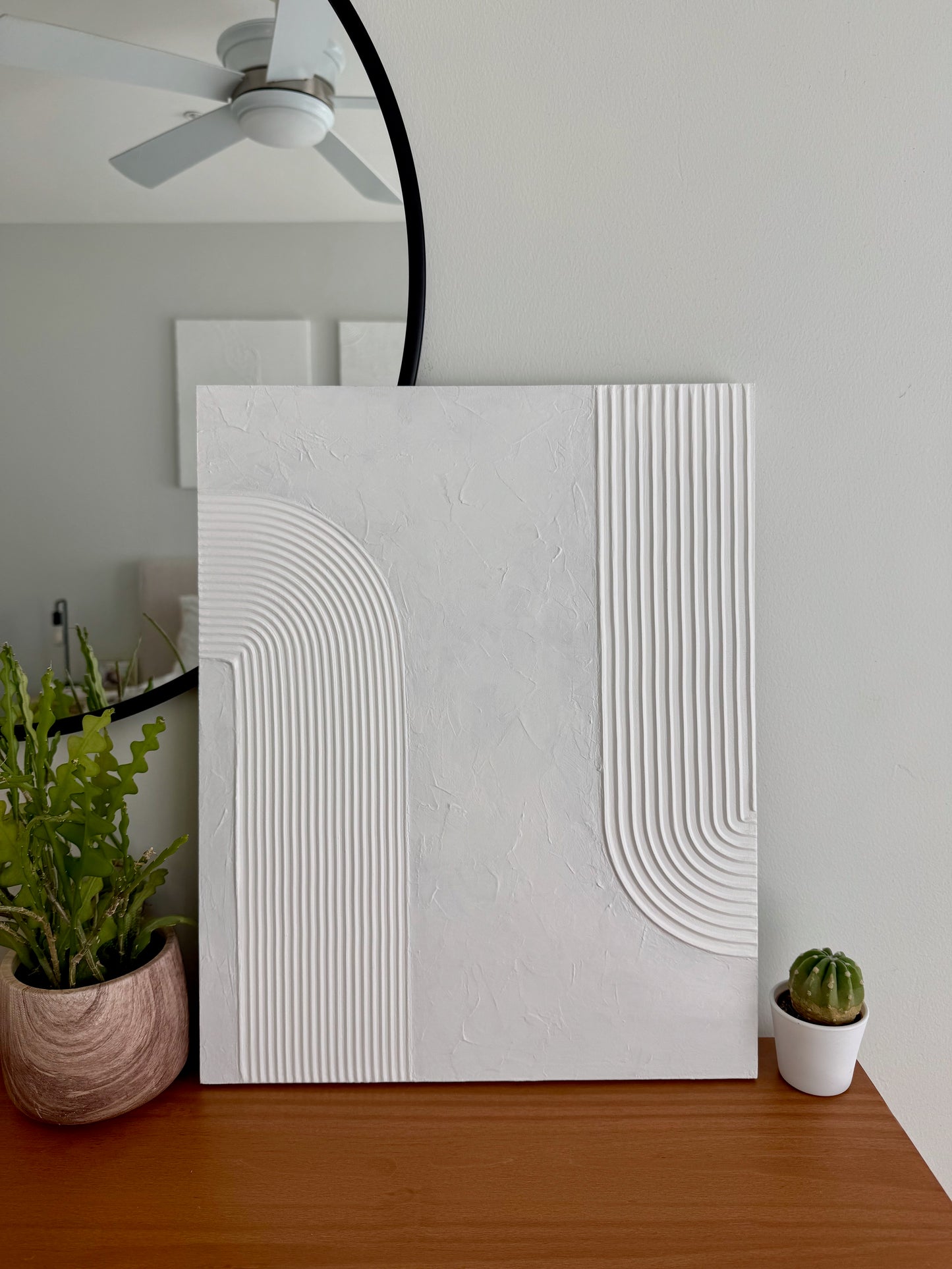 White textured wall art piece on a wooden surface with plants in the background