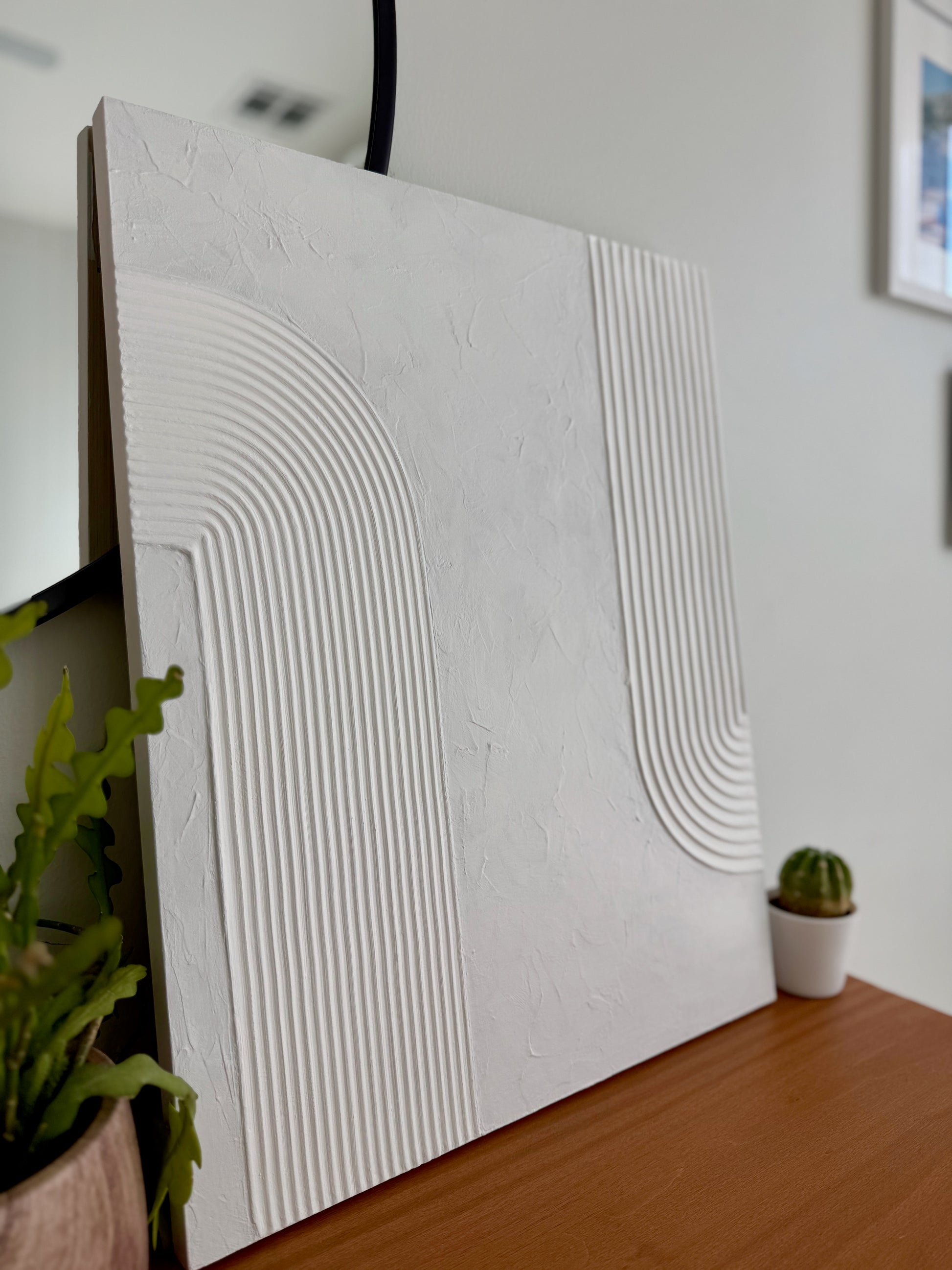 Textured white wall panel on a wooden surface with plants in the background