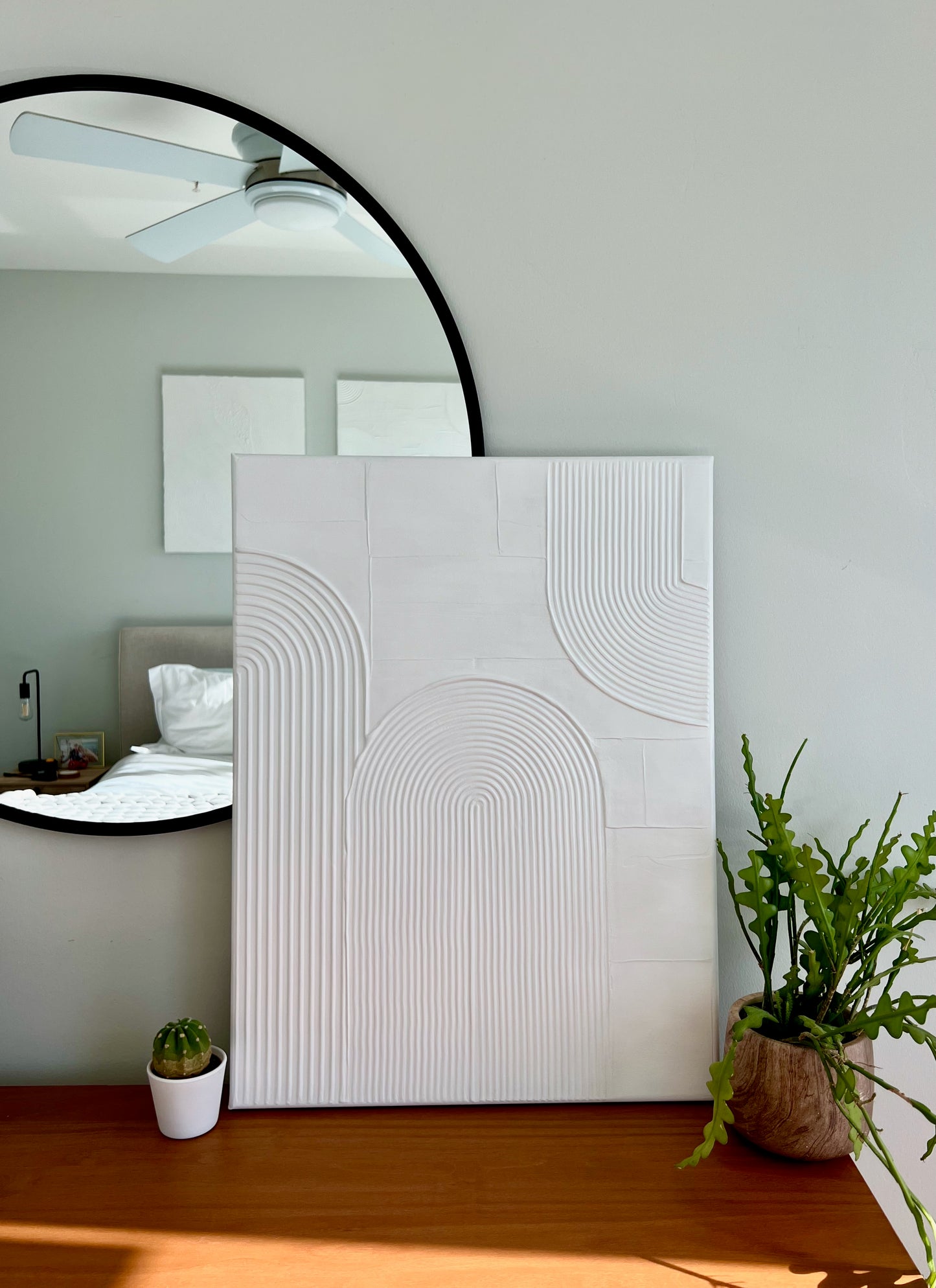 Modern interior with a large round mirror, abstract wall art, and potted plants.