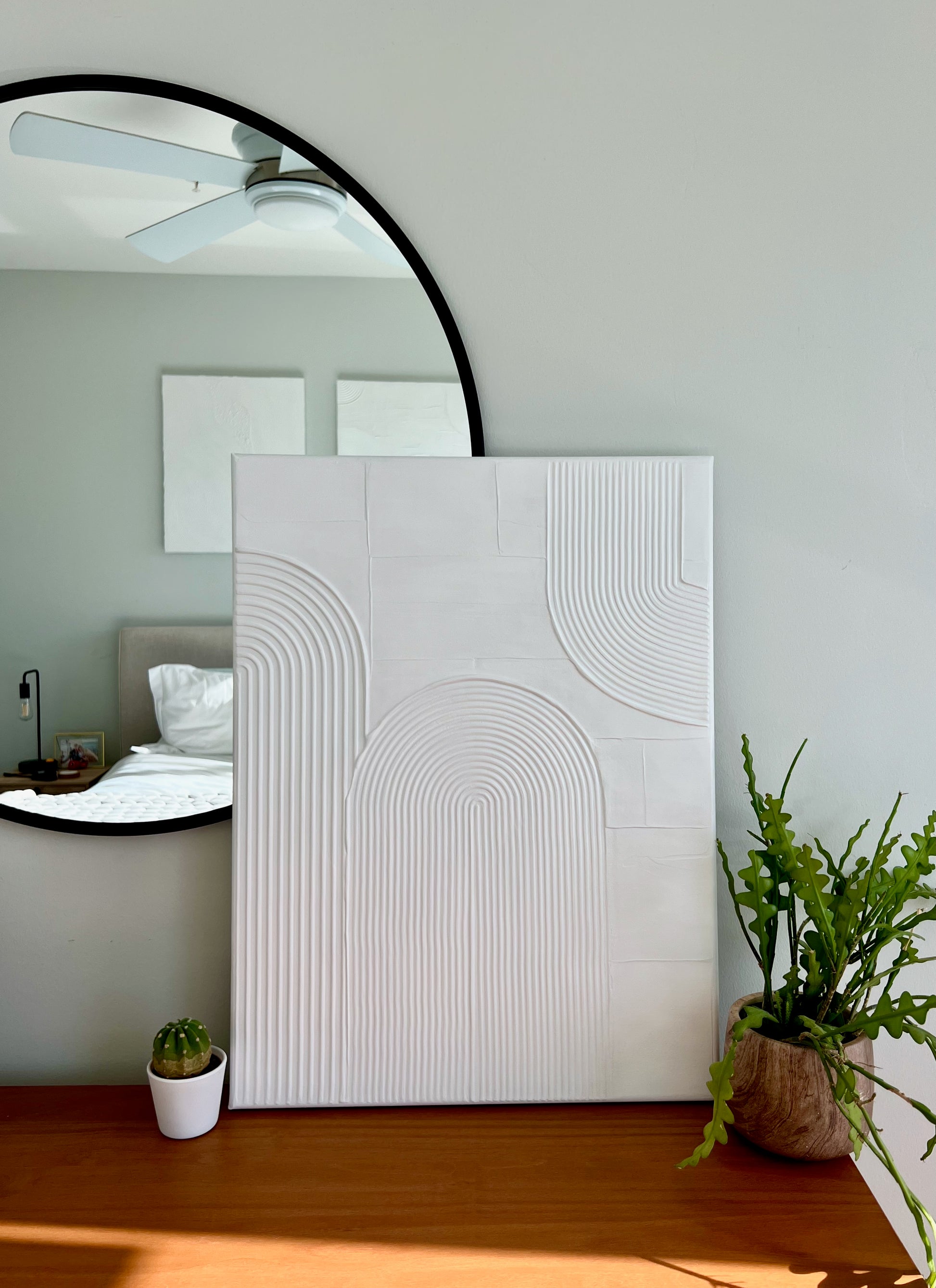 Modern interior with a large round mirror, abstract wall art, and potted plants.