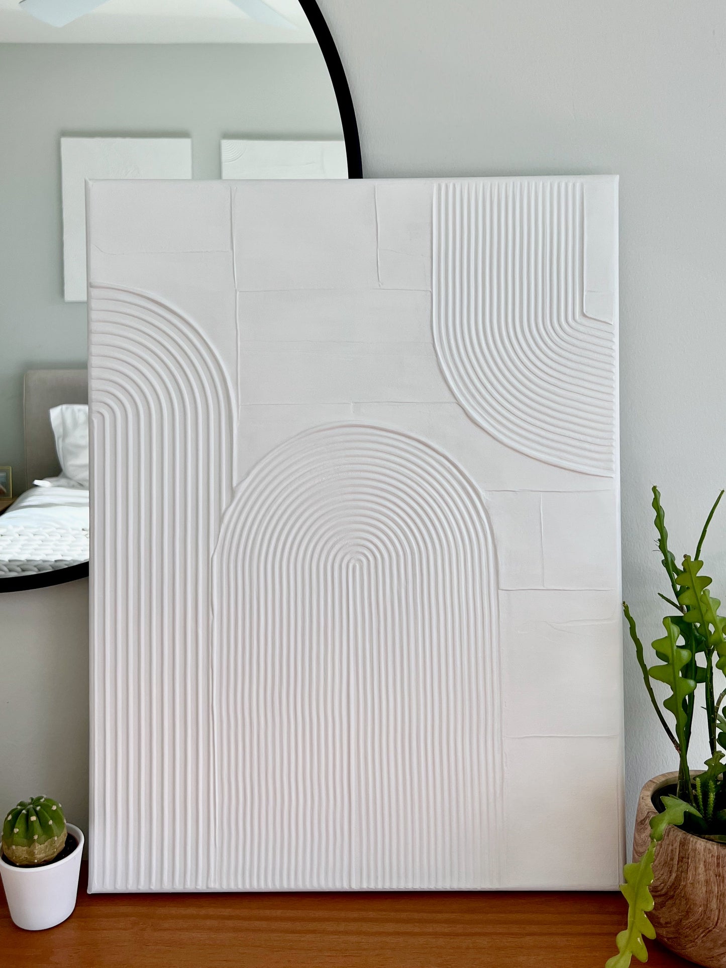 White textured wall art piece on a wooden shelf with decorative plants and a mirror.