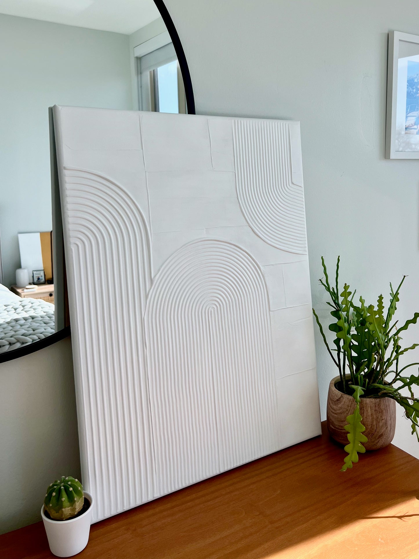 White textured wall art piece in a room with plants and a mirror.