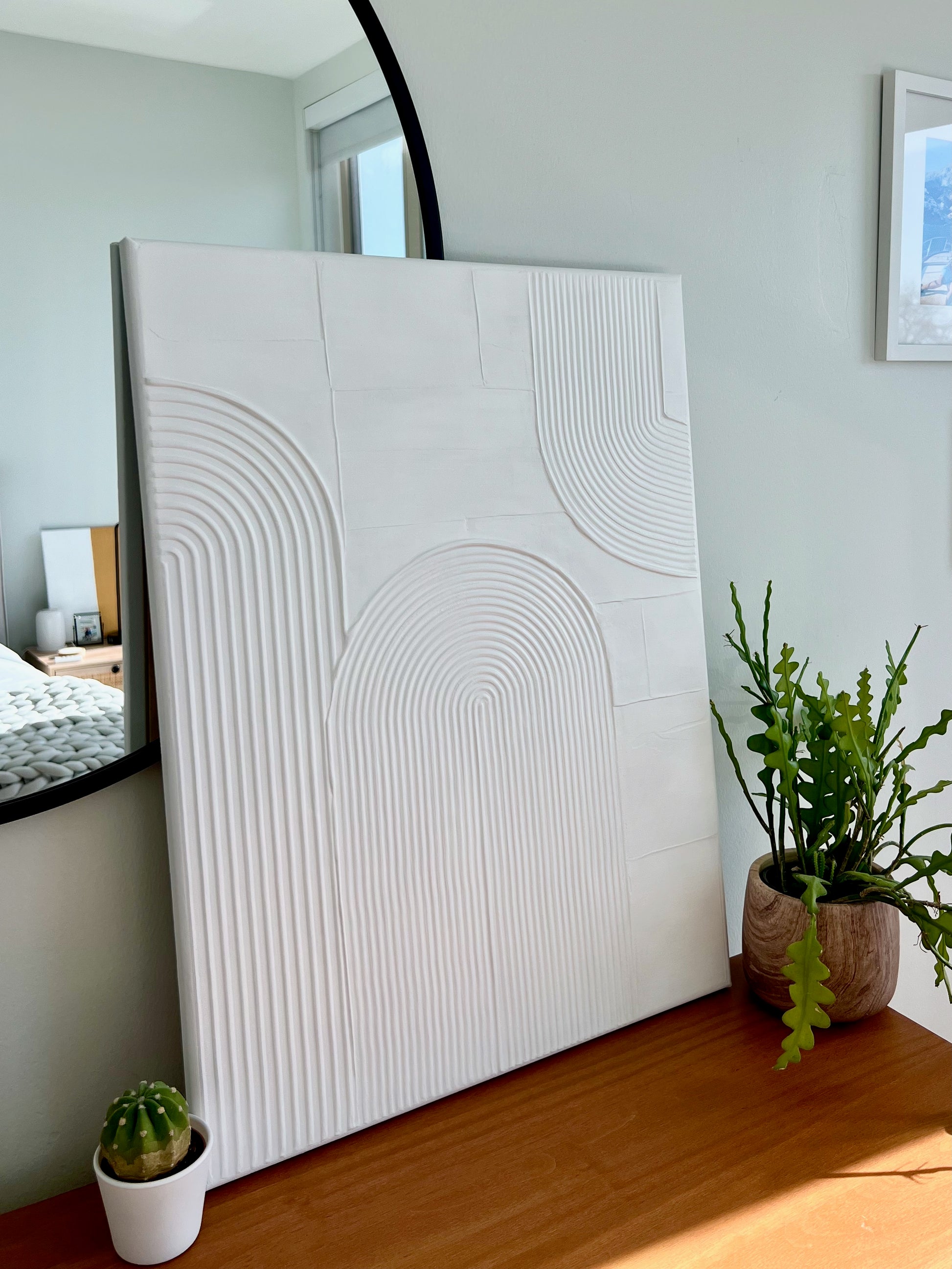White textured wall art piece in a room with plants and a mirror.