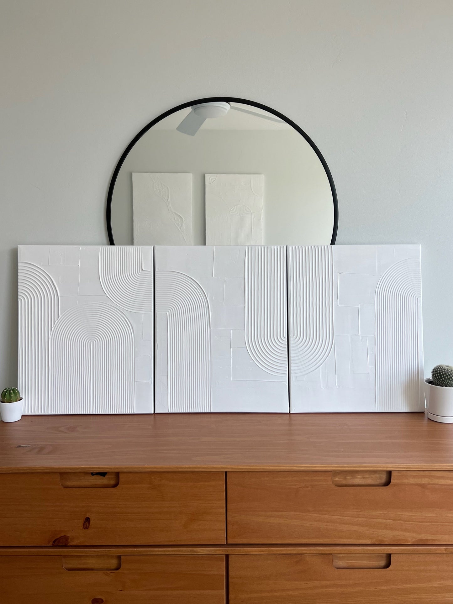 Wooden dresser with white textured wall panels and a round mirror above.
