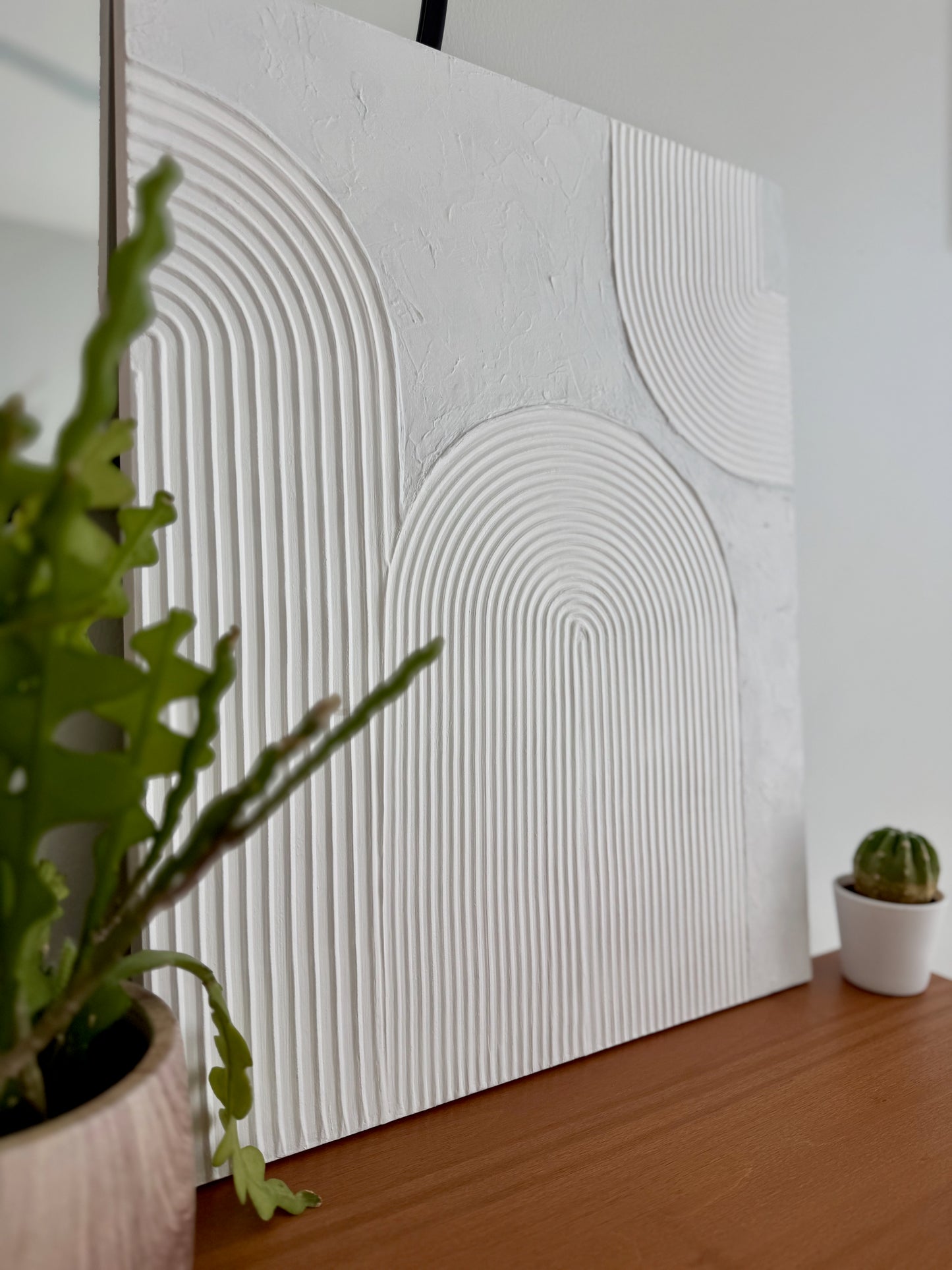 Textured wall panel with geometric pattern next to a potted plant on a wooden surface.