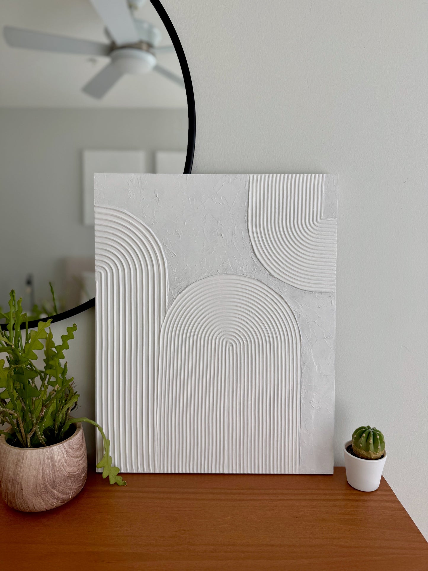Abstract wall art piece on a wooden surface with plants in the background