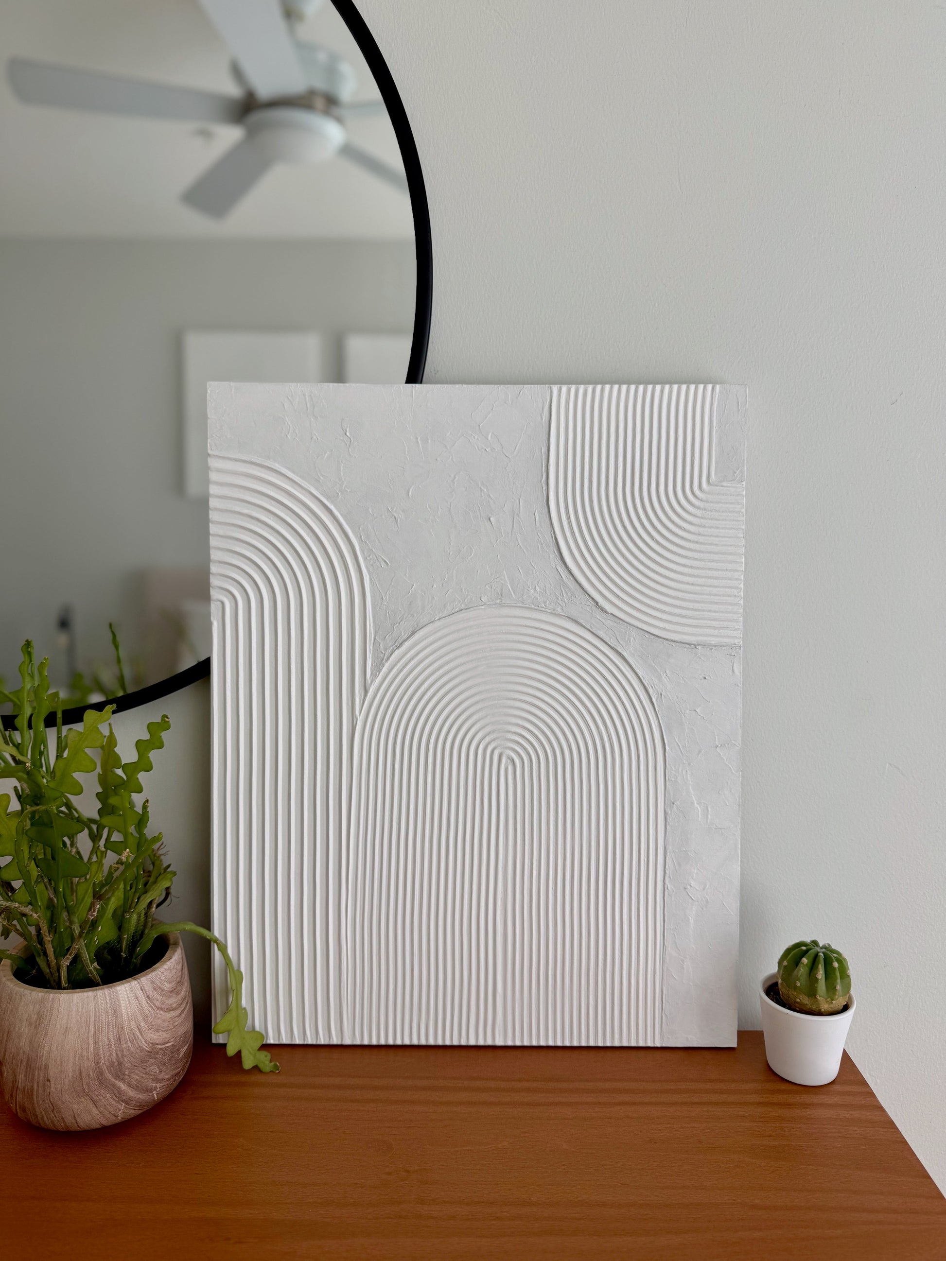 Abstract wall art piece on a wooden surface with plants in the background
