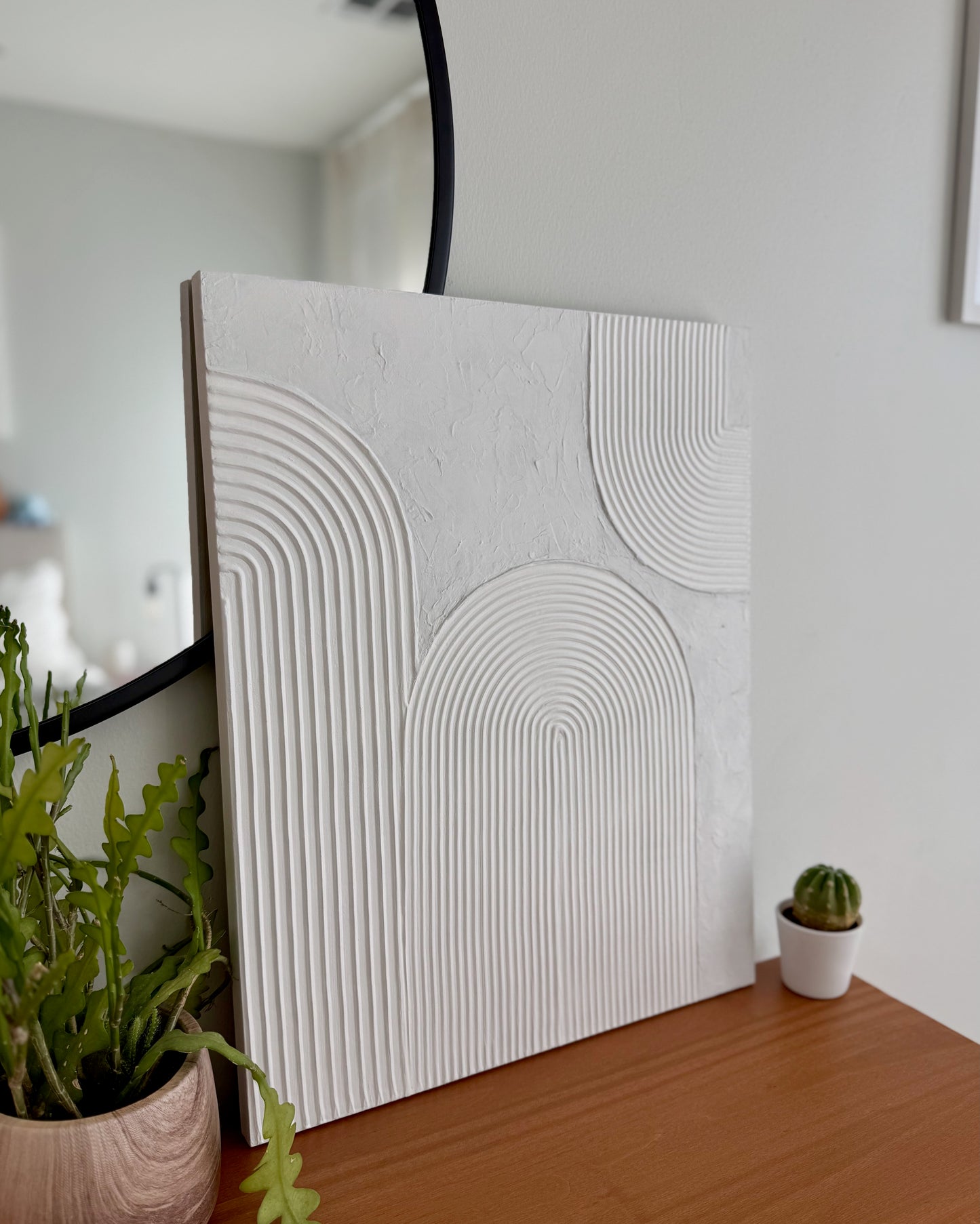 White textured wall panel on a wooden surface with plants in the background