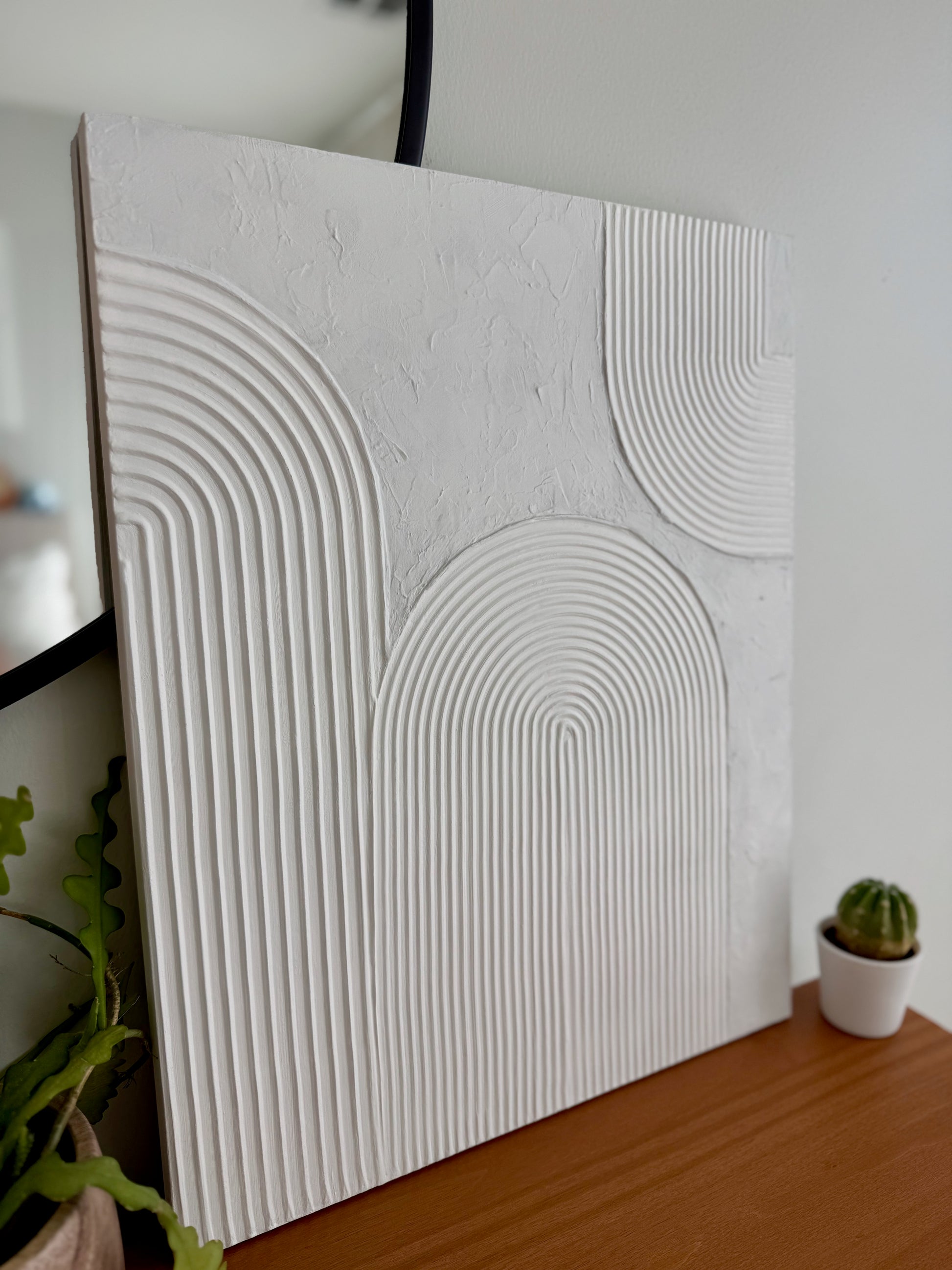 Textured white wall panel on a wooden surface with plants in the background