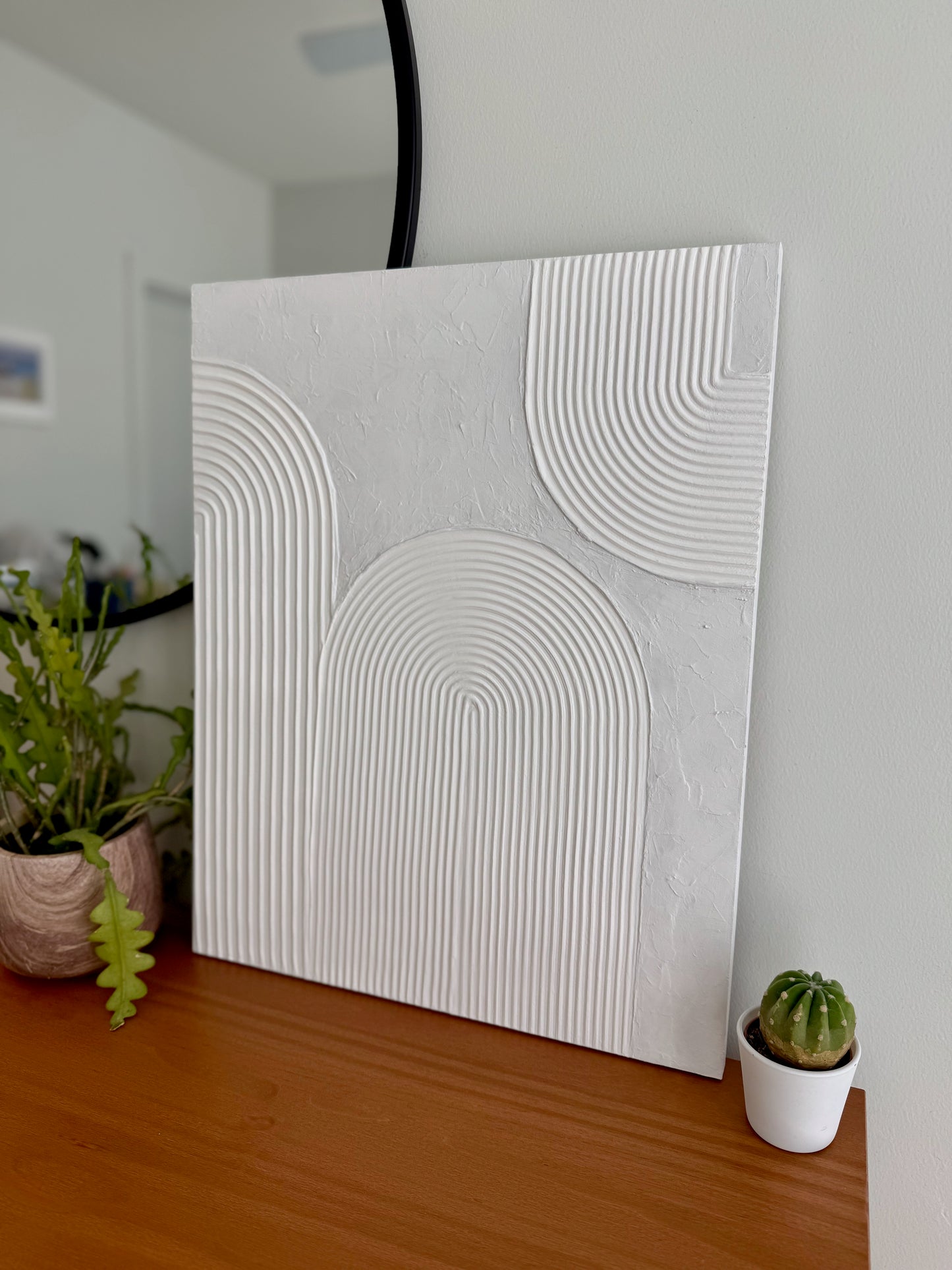 Abstract wall art piece on a wooden surface with plants in the background