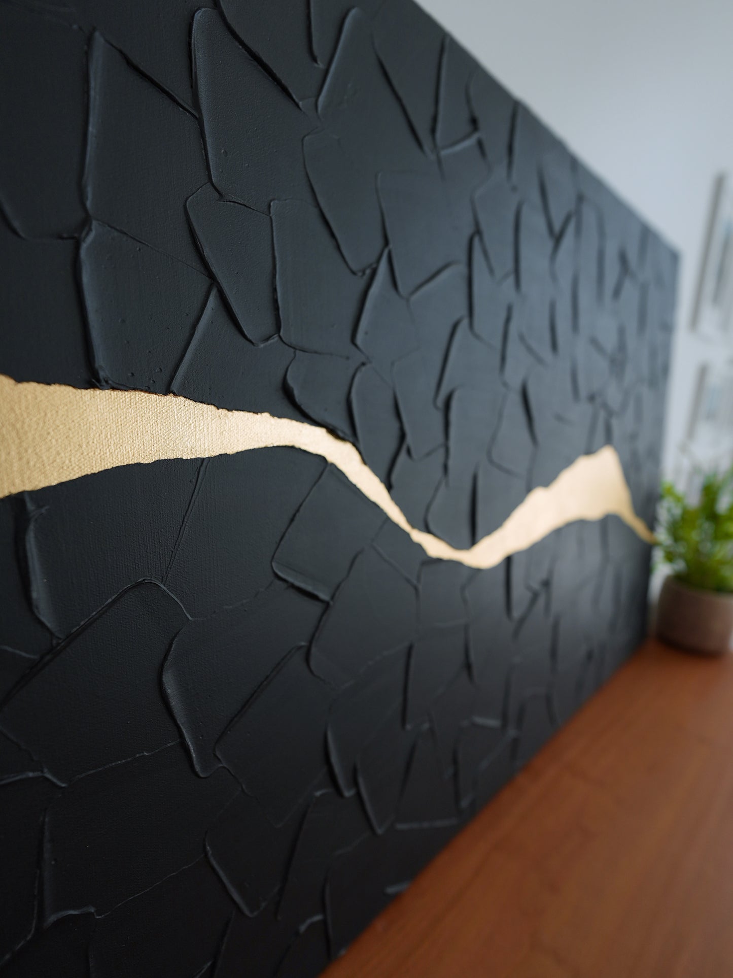 Black textured wall panel with a gold accent line in a room setting.
