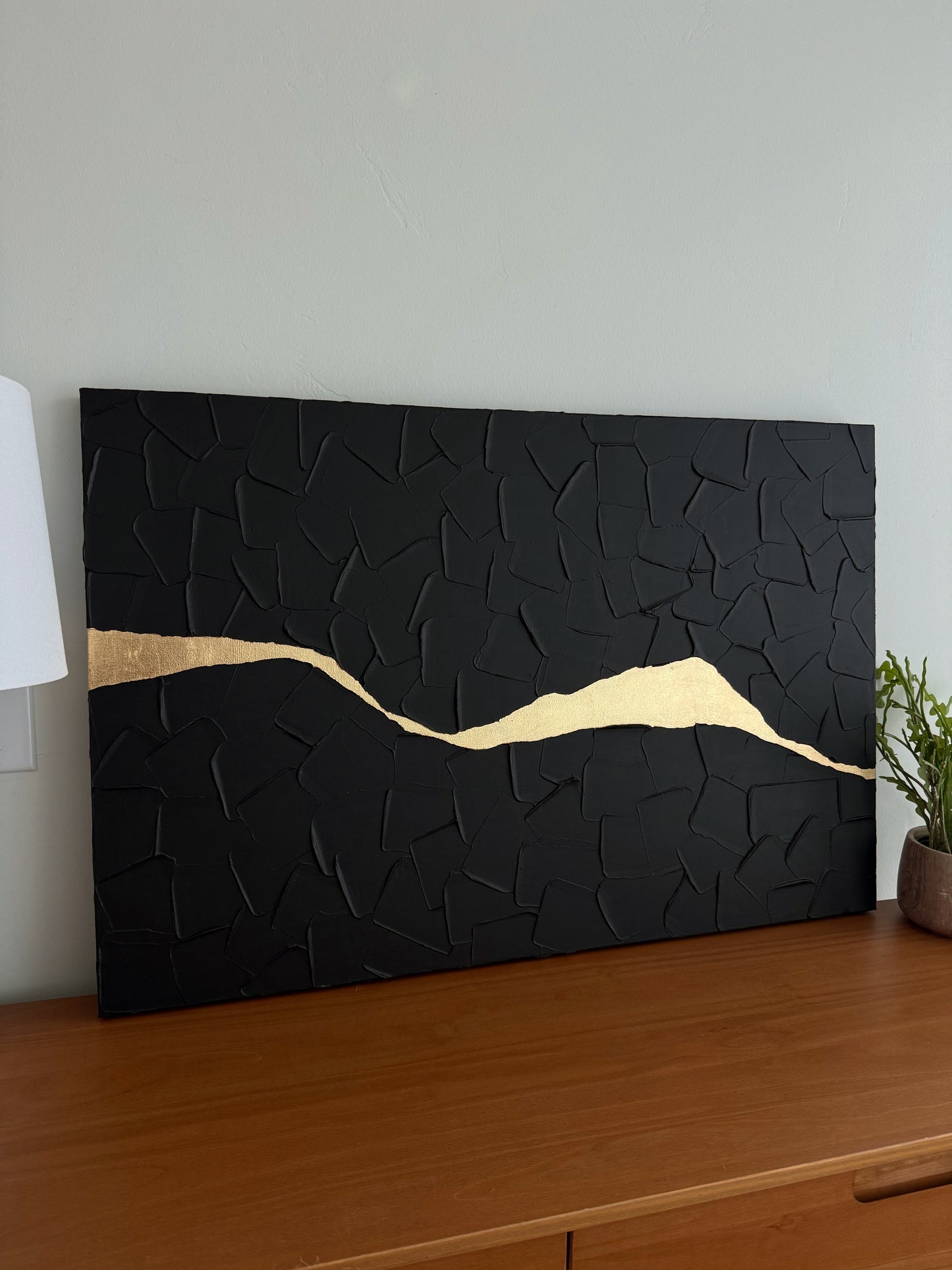 Black textured wall art with a gold accent on a wooden surface.