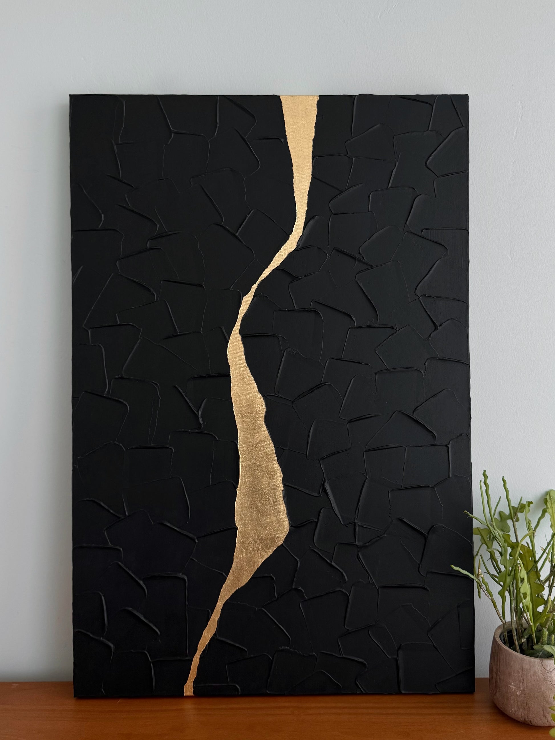 Black textured wall art with a gold accent on a white wall