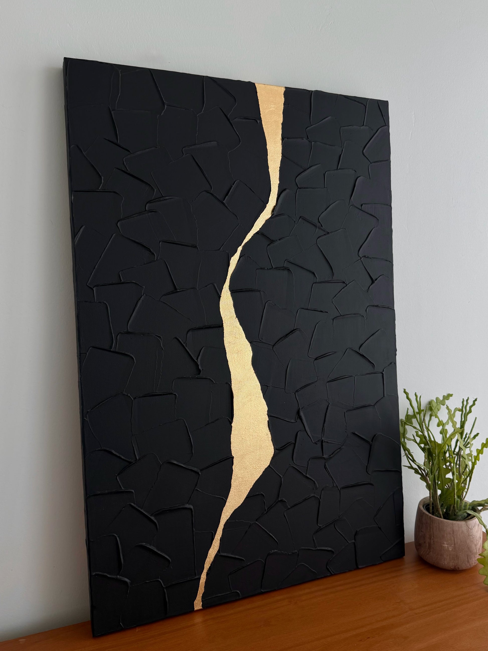 Black textured wall art with a gold accent on a wooden surface.