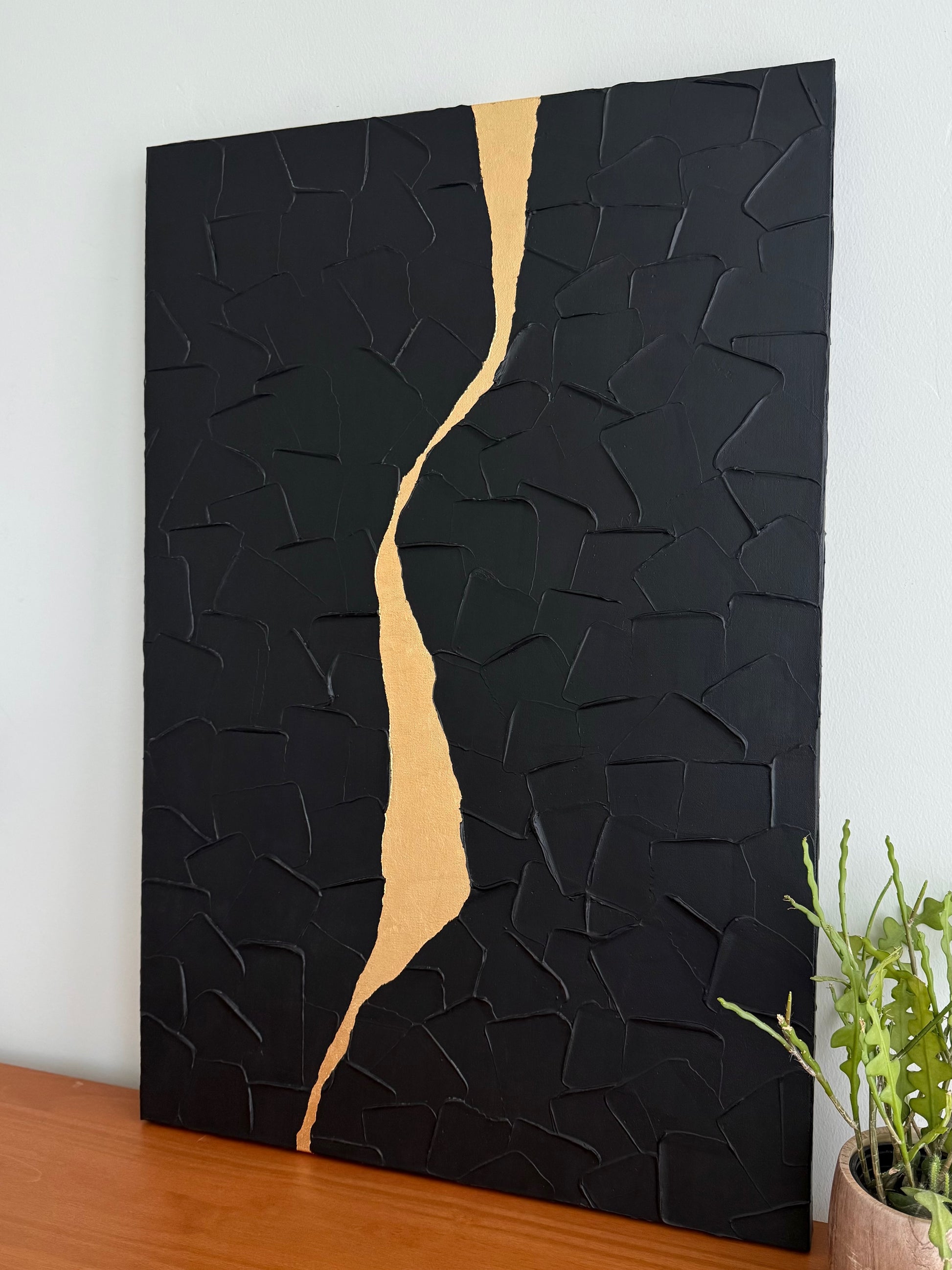 Abstract art piece with black and gold design on a white wall