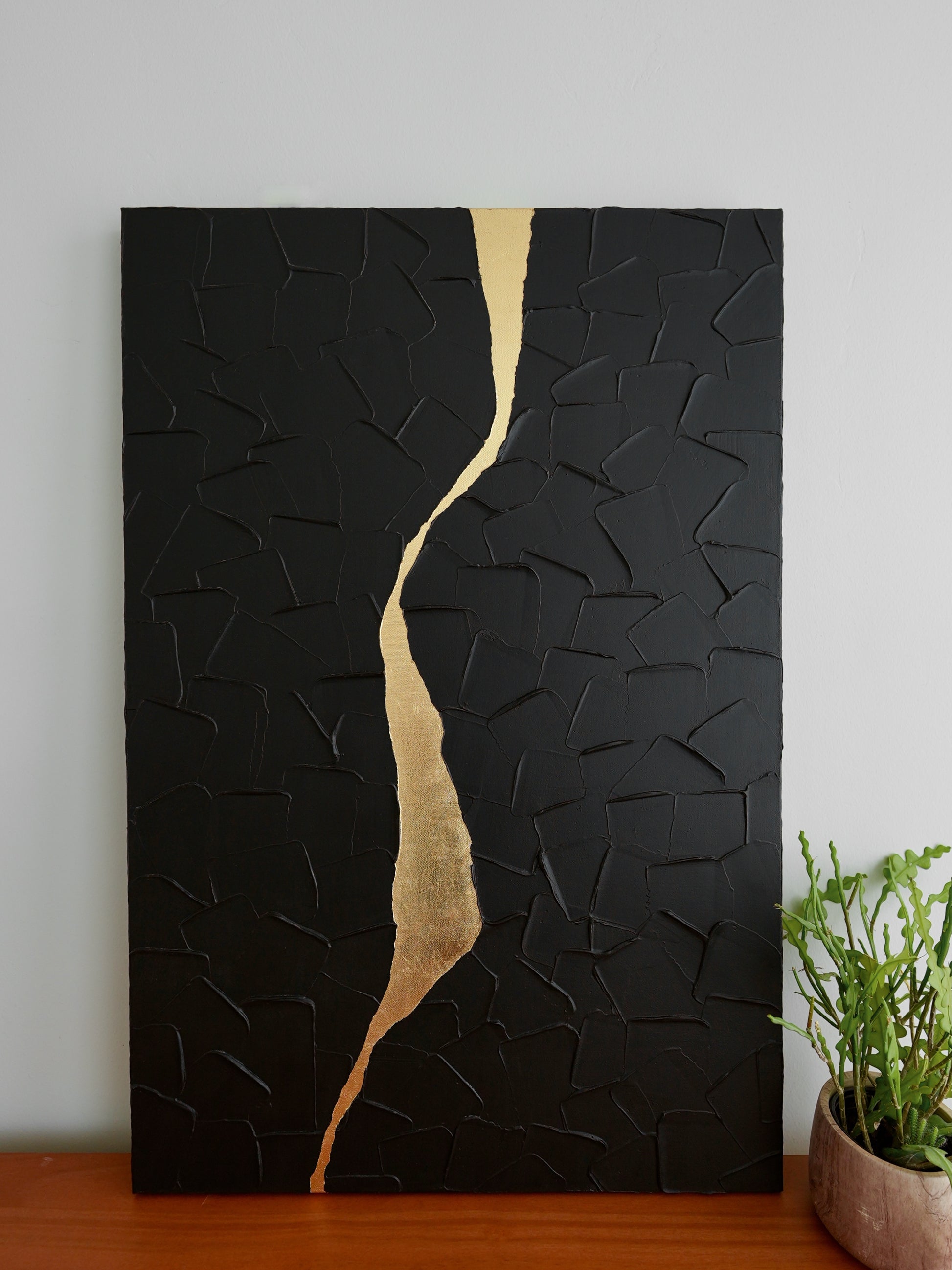 Black textured wall art with a gold accent on a white wall