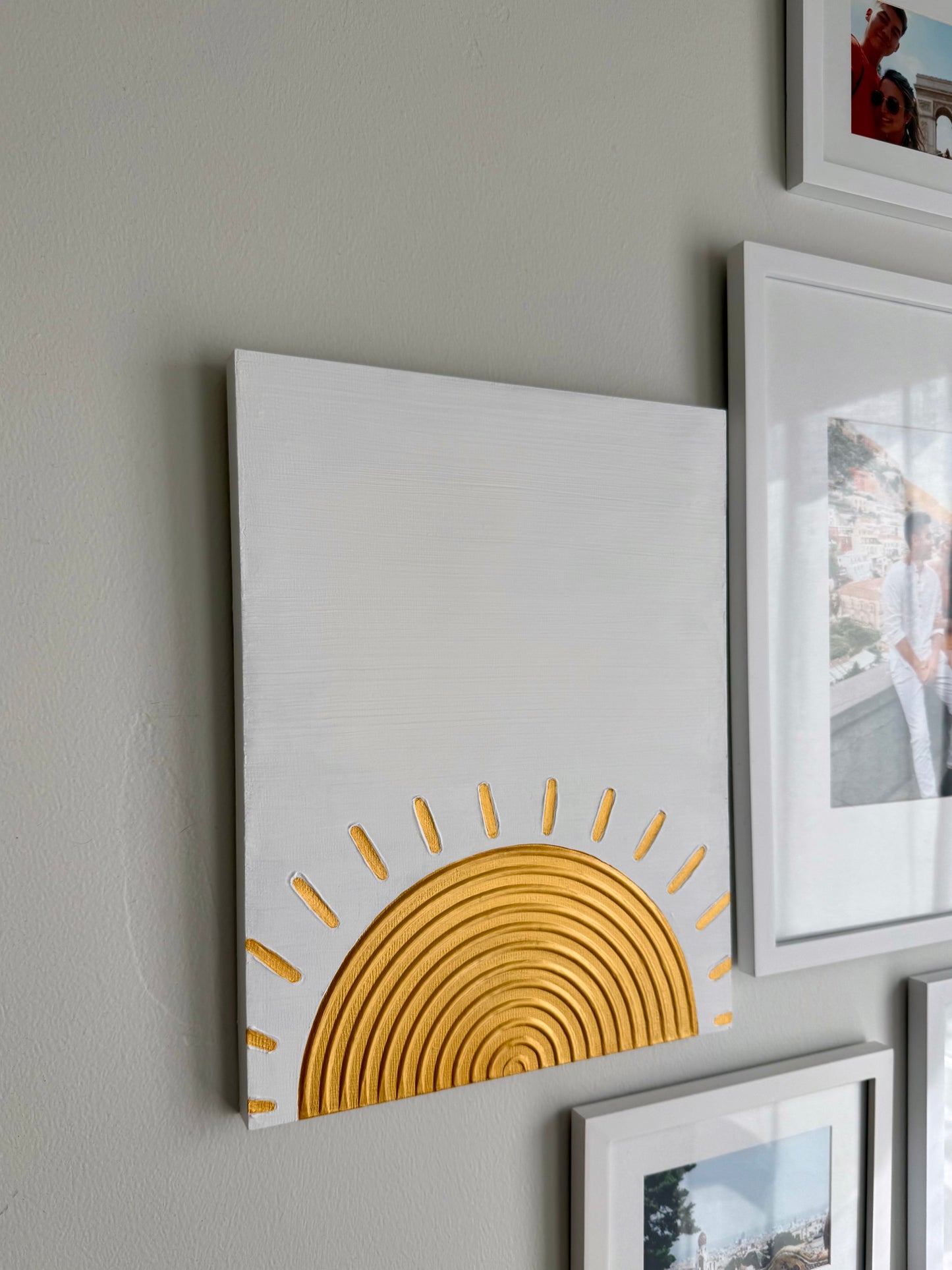 Decorative wall art with a yellow sun design on a white background, surrounded by other framed pictures.