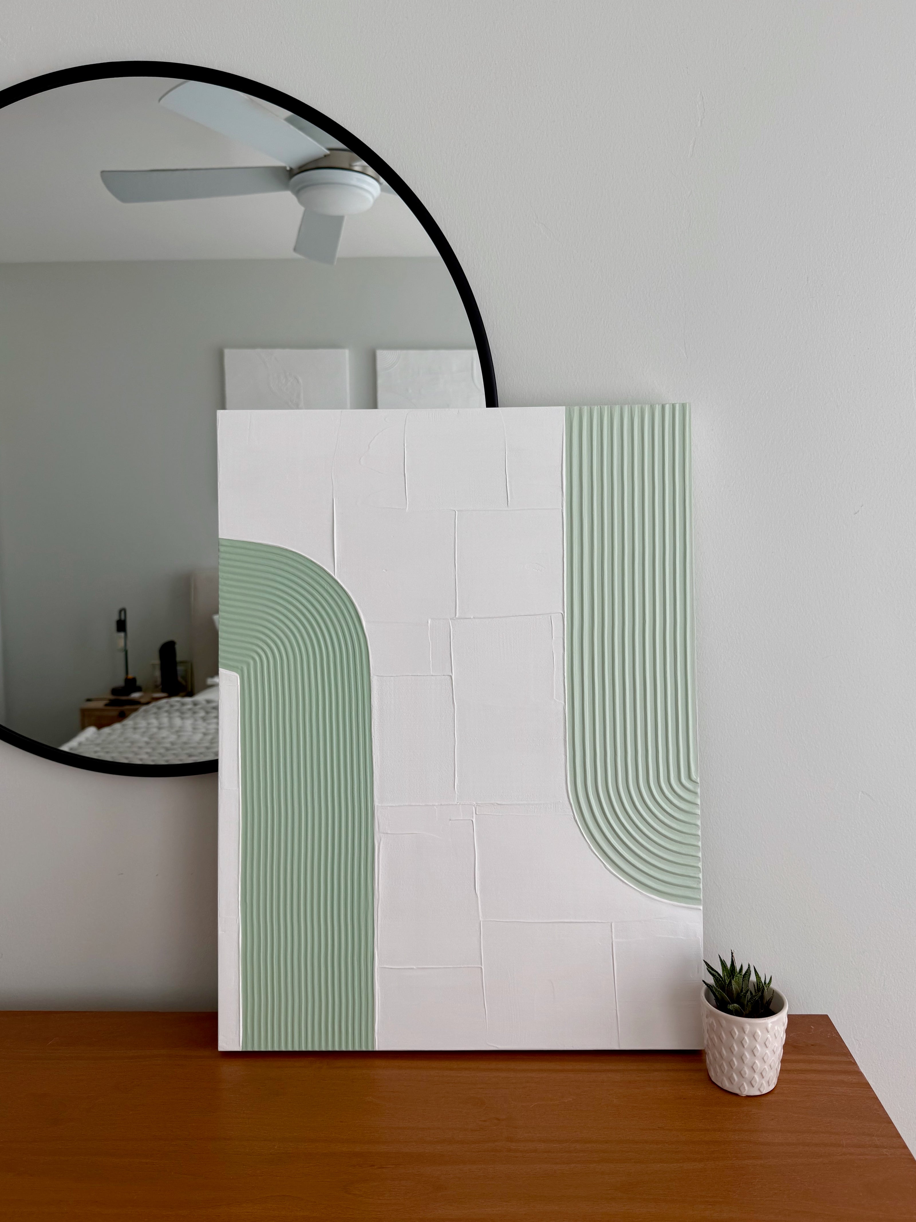 Modern interior design with a large round mirror, abstract wall art, and a small plant on a wooden surface.