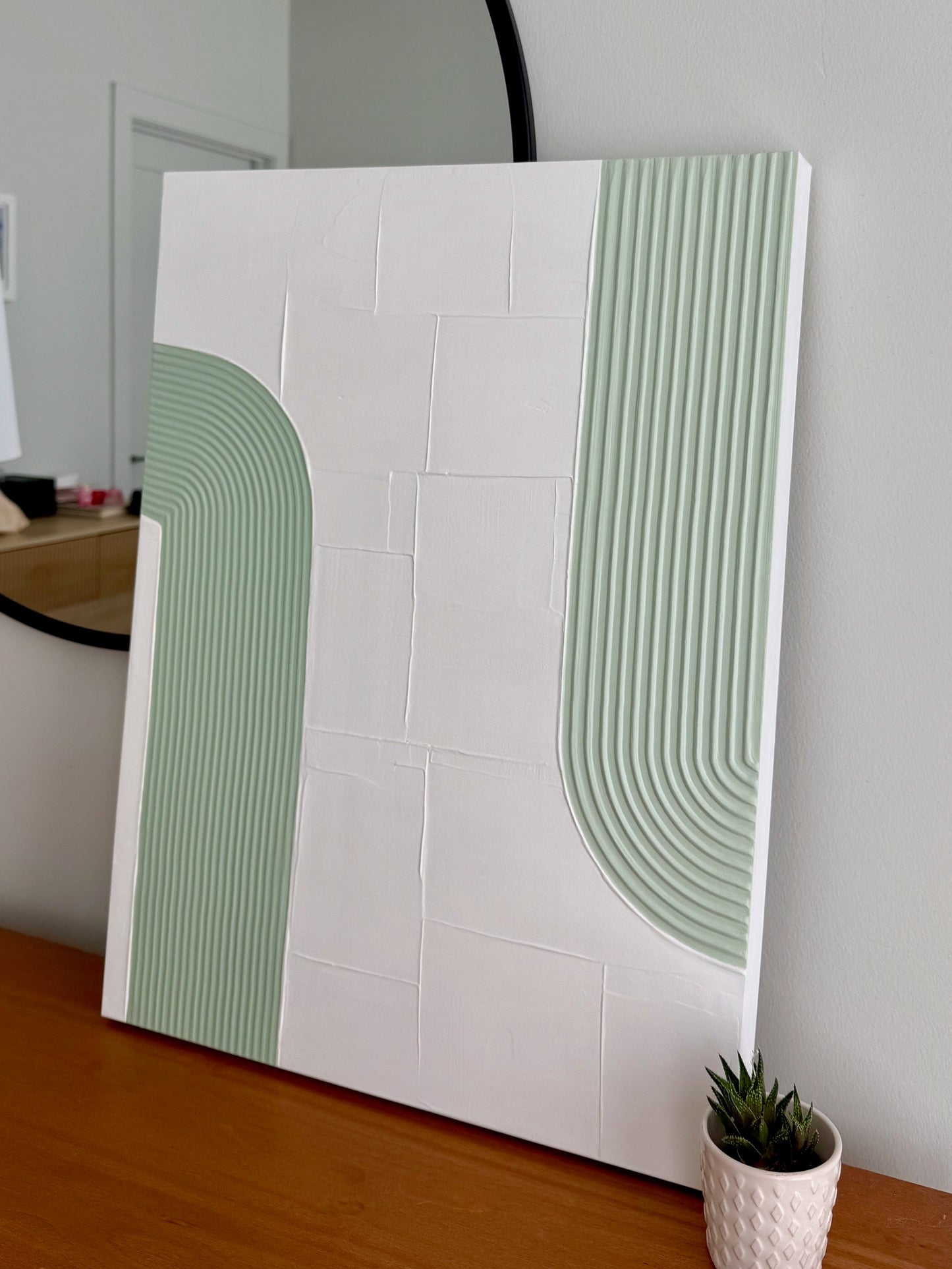 White wall with green geometric patterns and a small plant on a wooden surface.