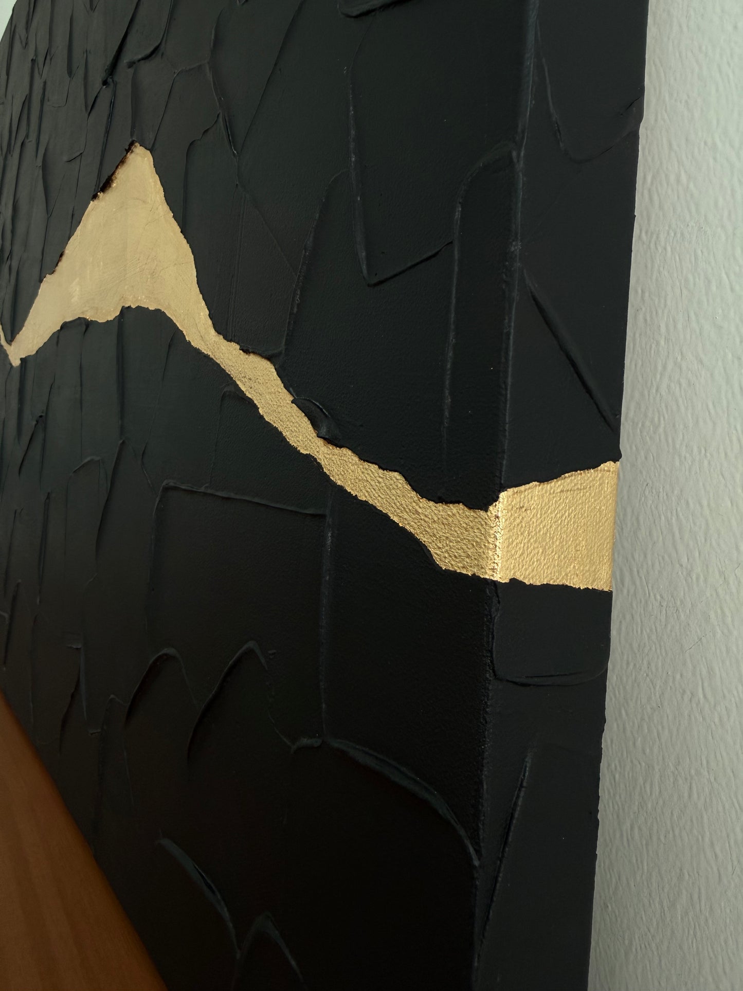 Black textured wall art with a gold accent line on a white wall.