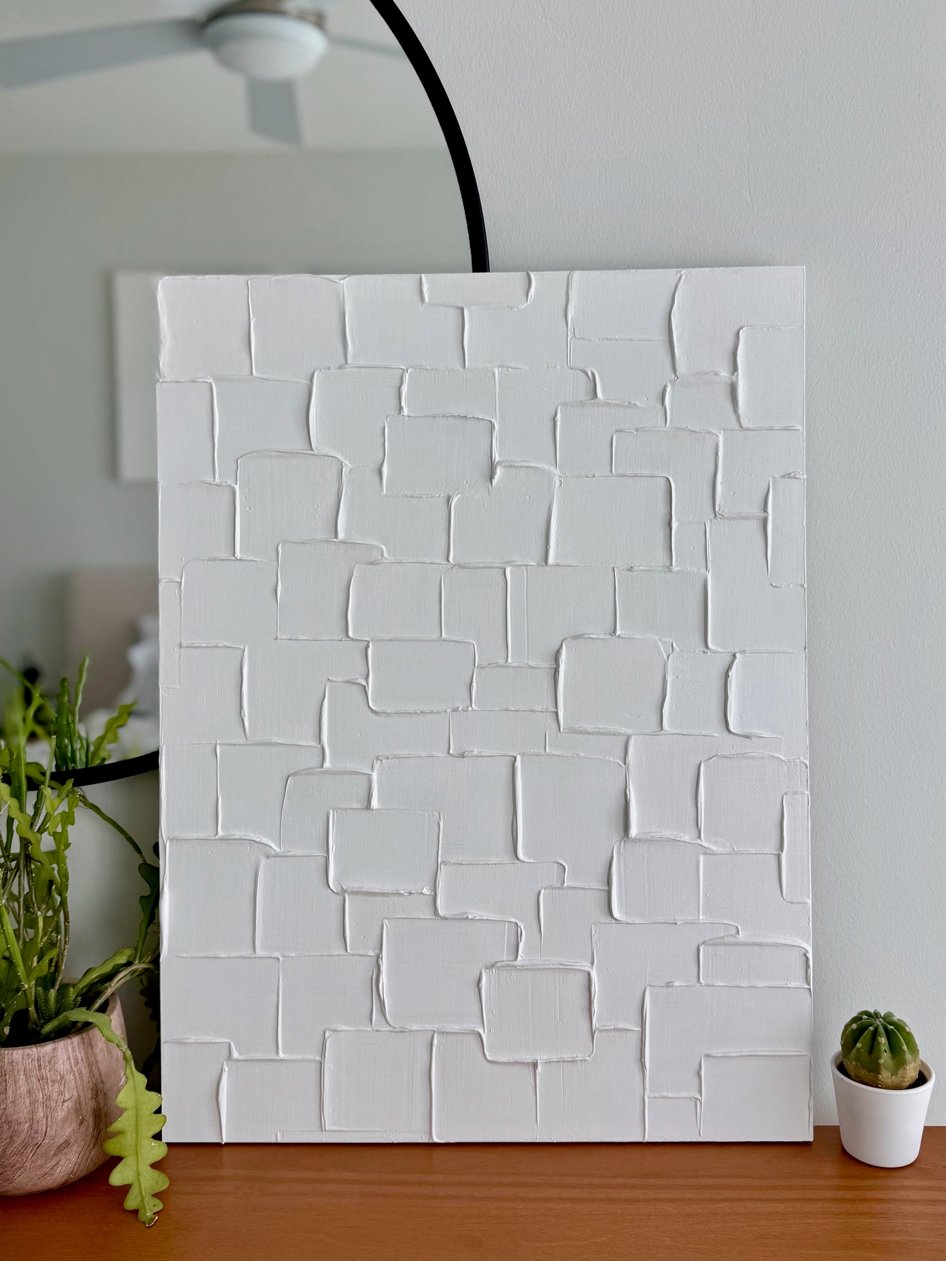 White textured wall panel in a room with plants and a ceiling fan.