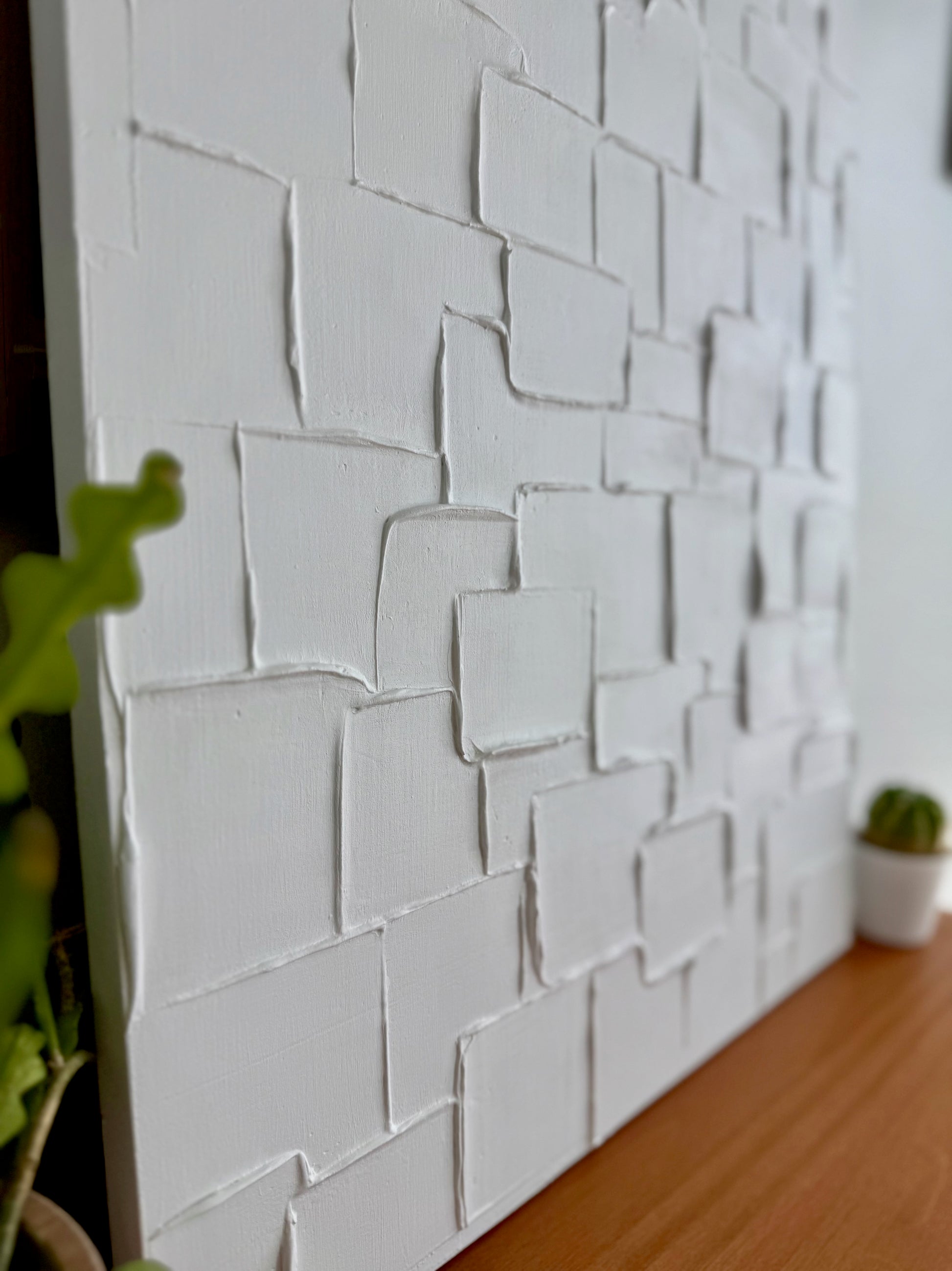 Textured white wall panel with a plant on a wooden surface