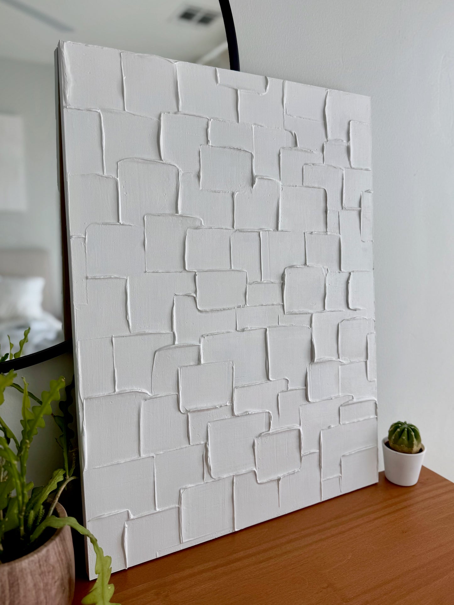 White textured wall panel on a wooden surface with plants in the background