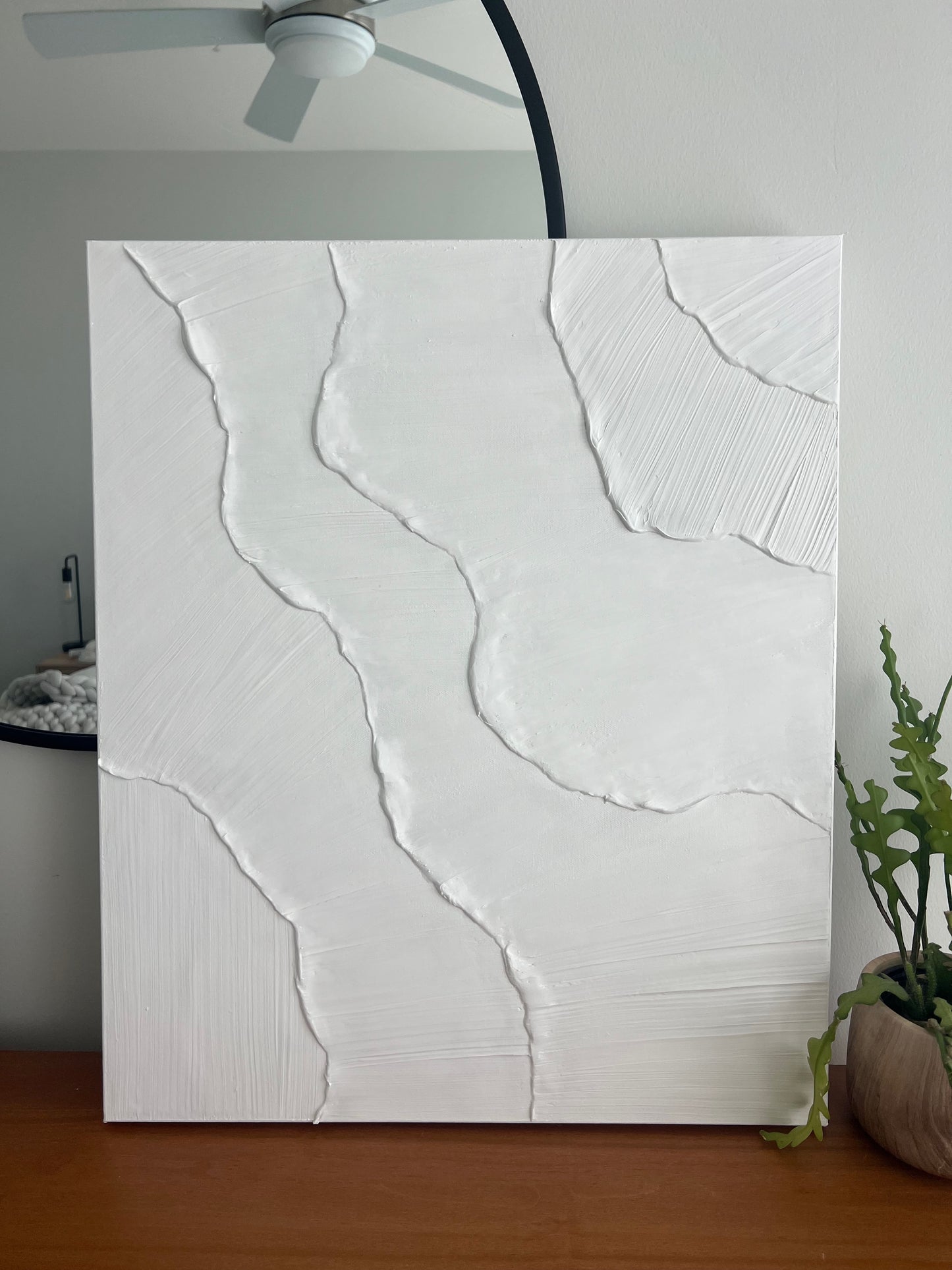 Abstract white painting on a wooden surface with a plant in the background