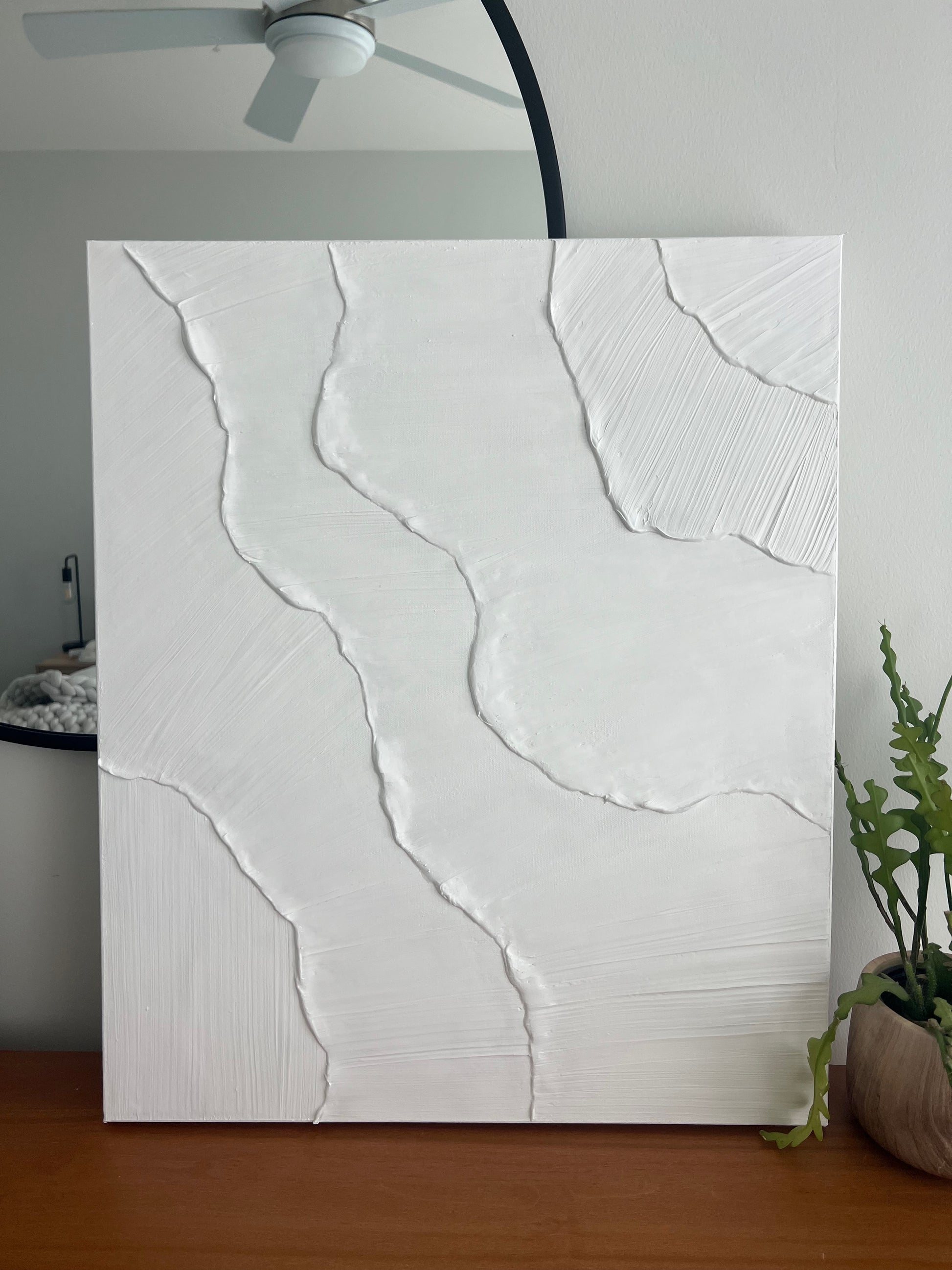 Abstract white painting on a wooden surface with a plant in the background