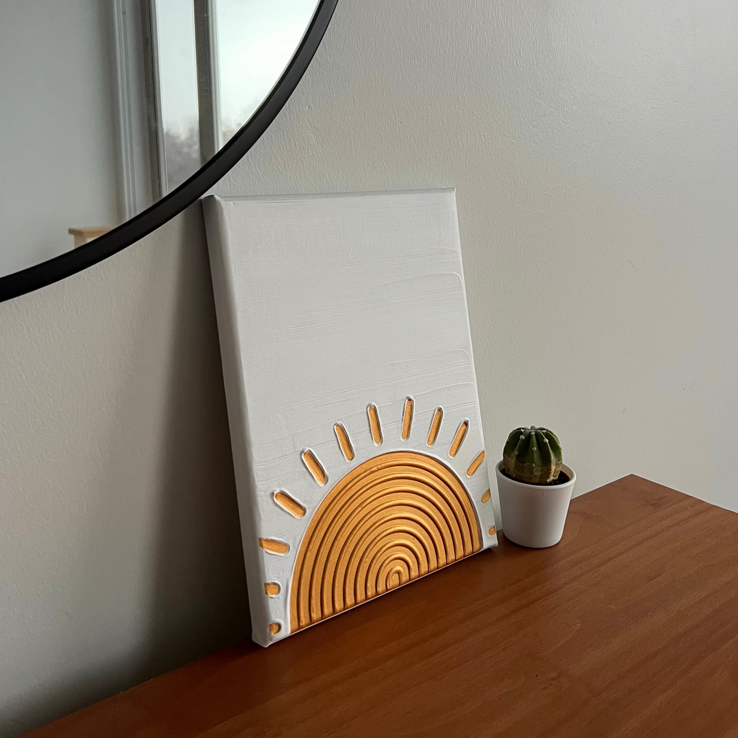 small canvas with a gold sun textured art design on top of a dresser