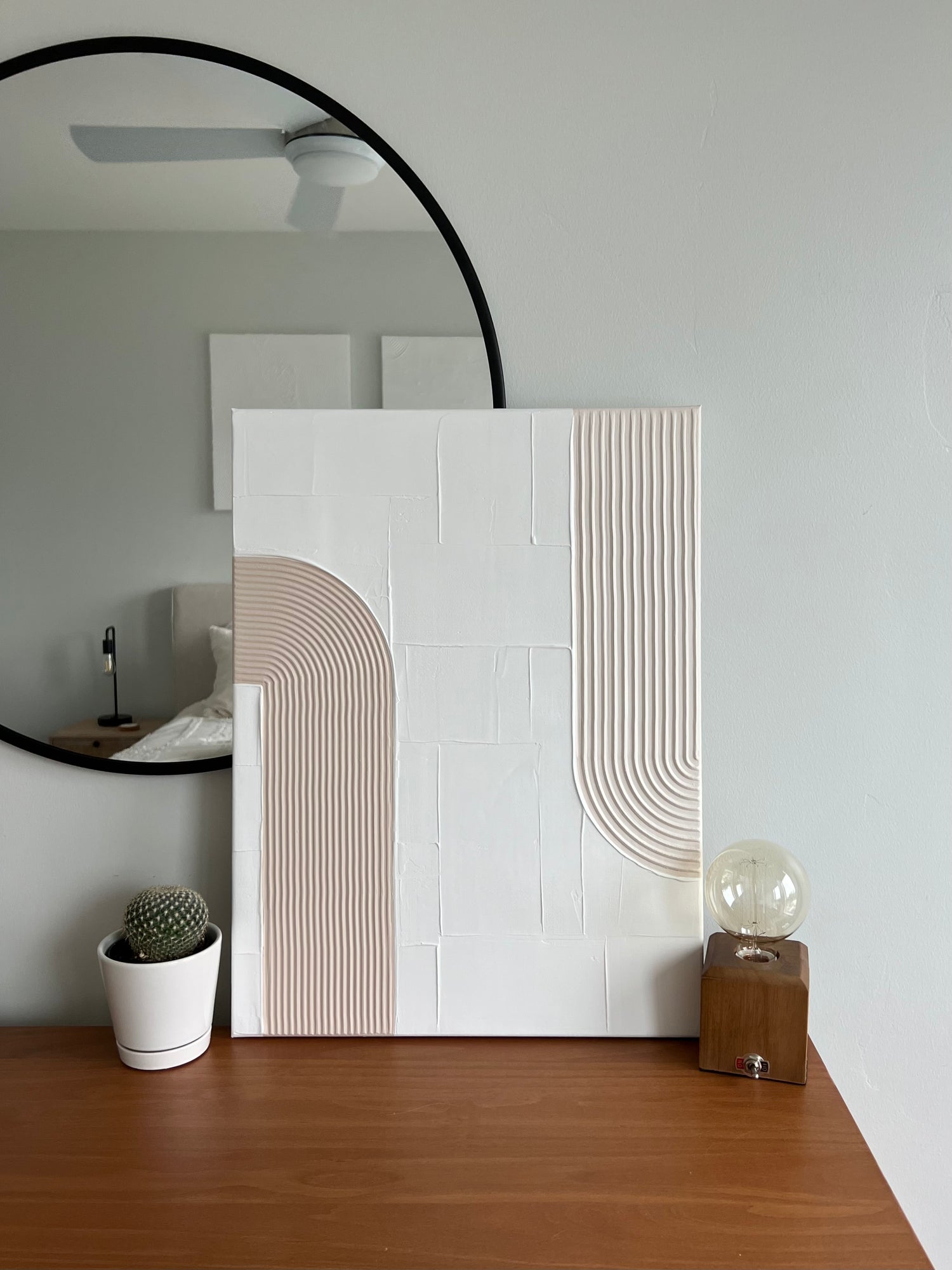 Decorative wall art with geometric design on a wooden surface, next to a round mirror.