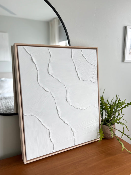 Framed abstract artwork on a wooden surface with a plant in the background